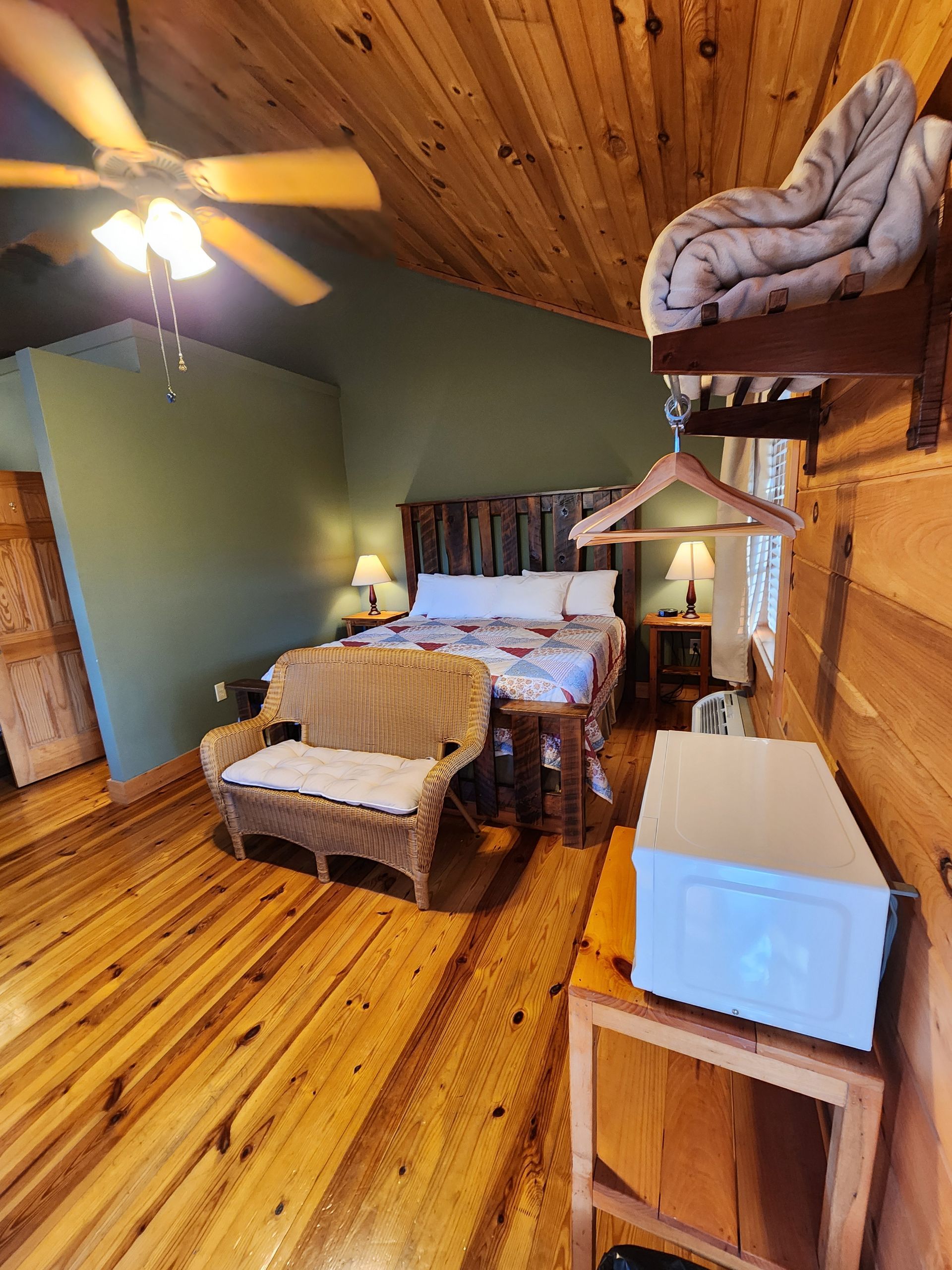Bedroom with wooden floors, ceiling, and walls, bed, wicker bench, and shelving.