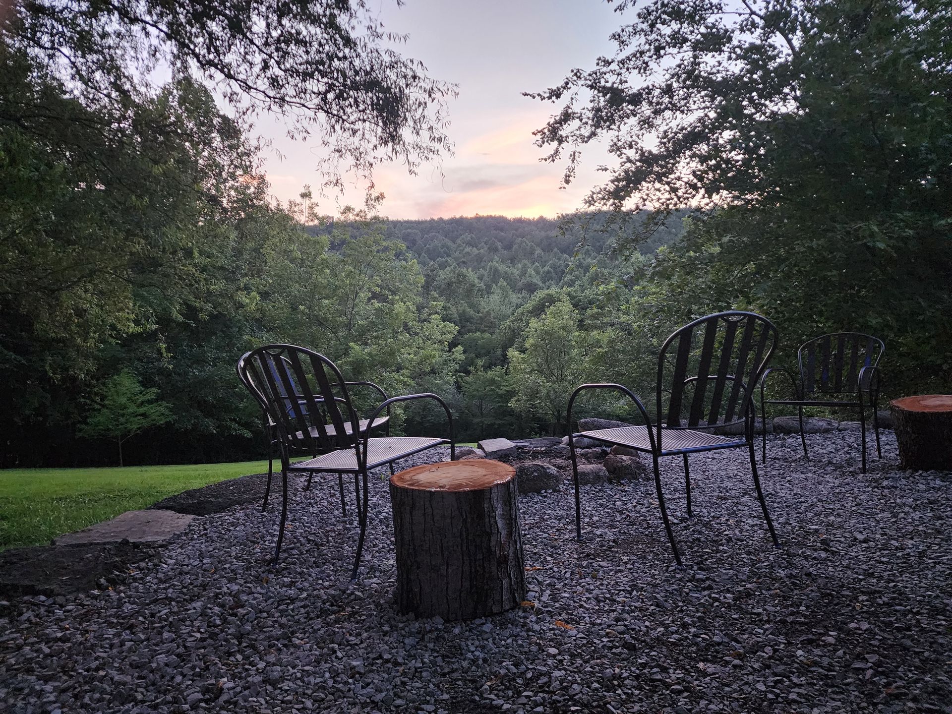 Two metal chairs and a tree stump overlook a forested valley at dusk.