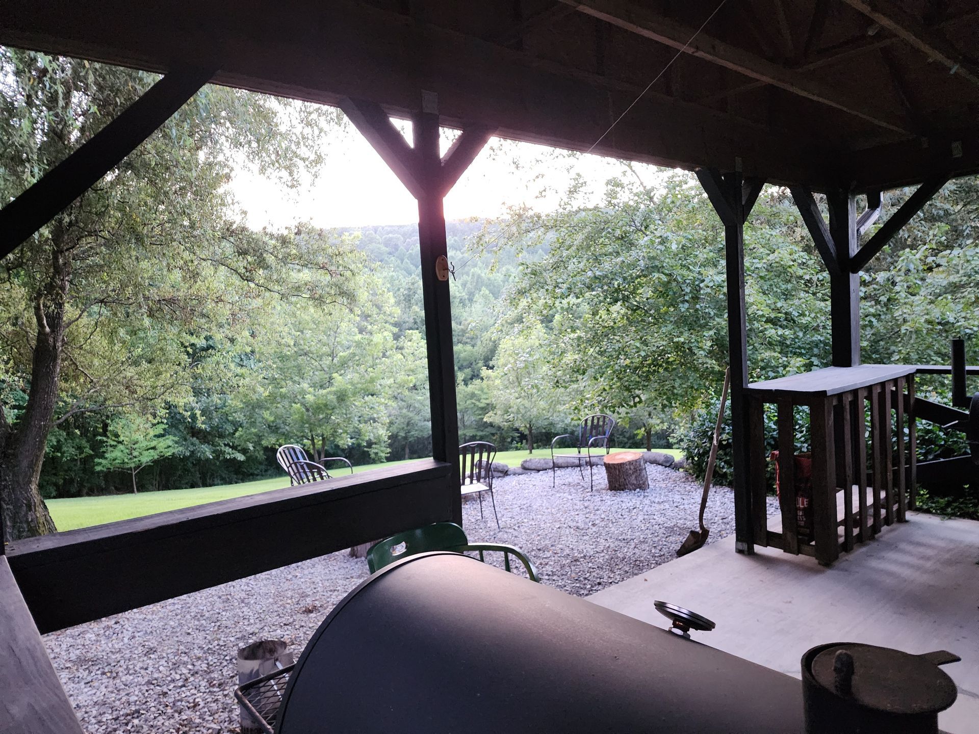Covered porch overlooking a forested valley with a barbecue grill in foreground.