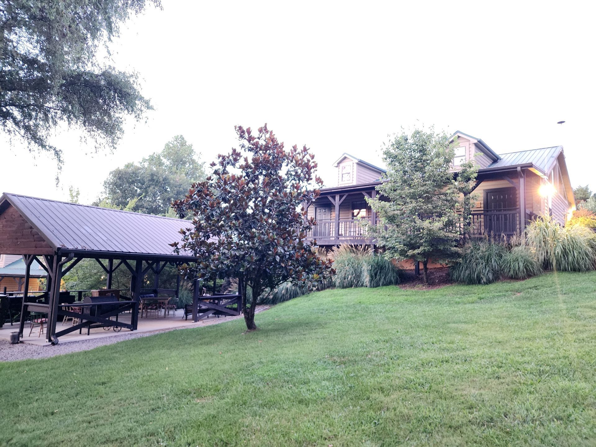 Lawn with a covered picnic area and a two-story building in the background. Evening light.