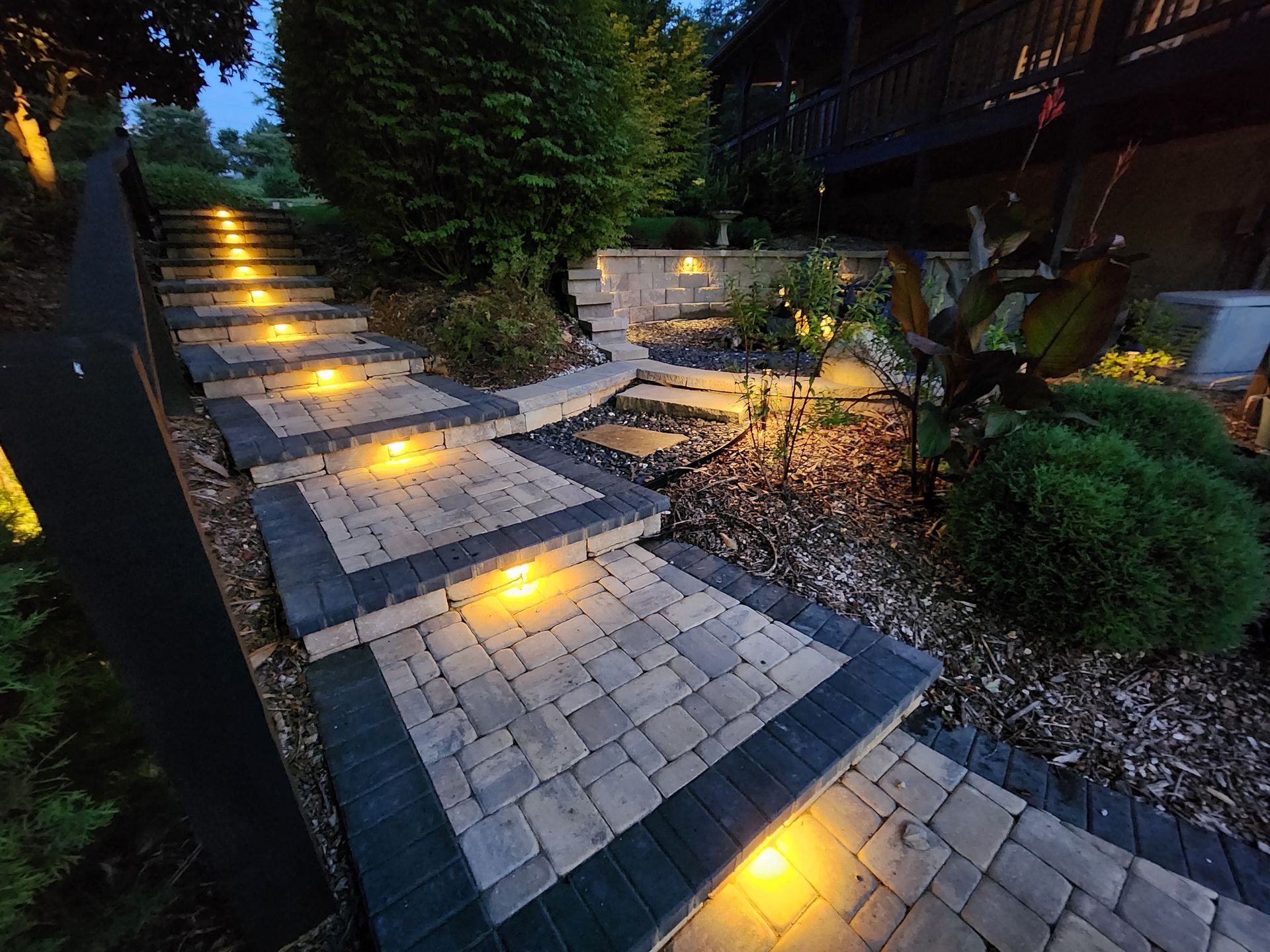 Lit stone steps lead up a garden path at dusk.