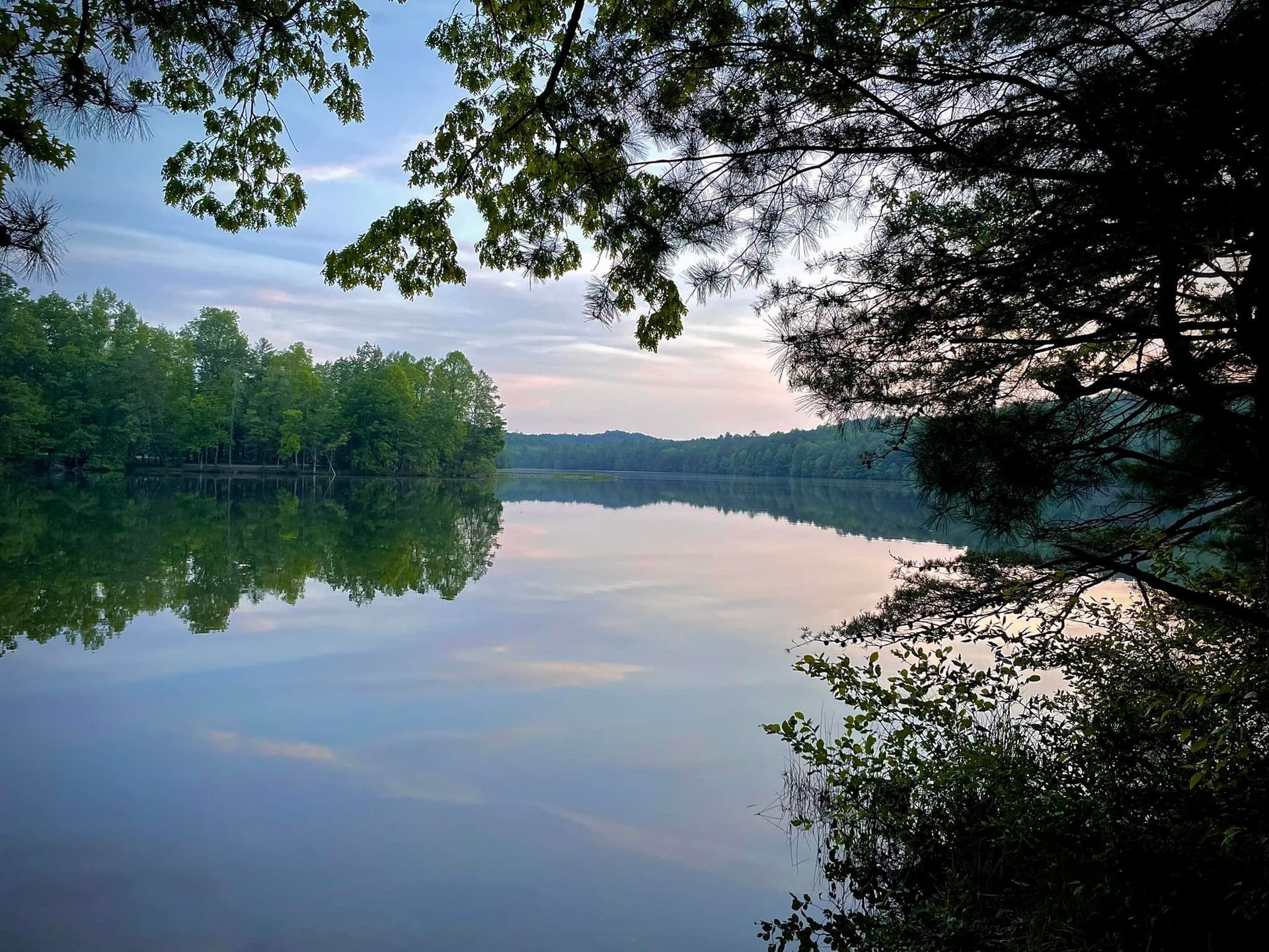Tranquil lake at dusk reflecting the sky and surrounding trees.