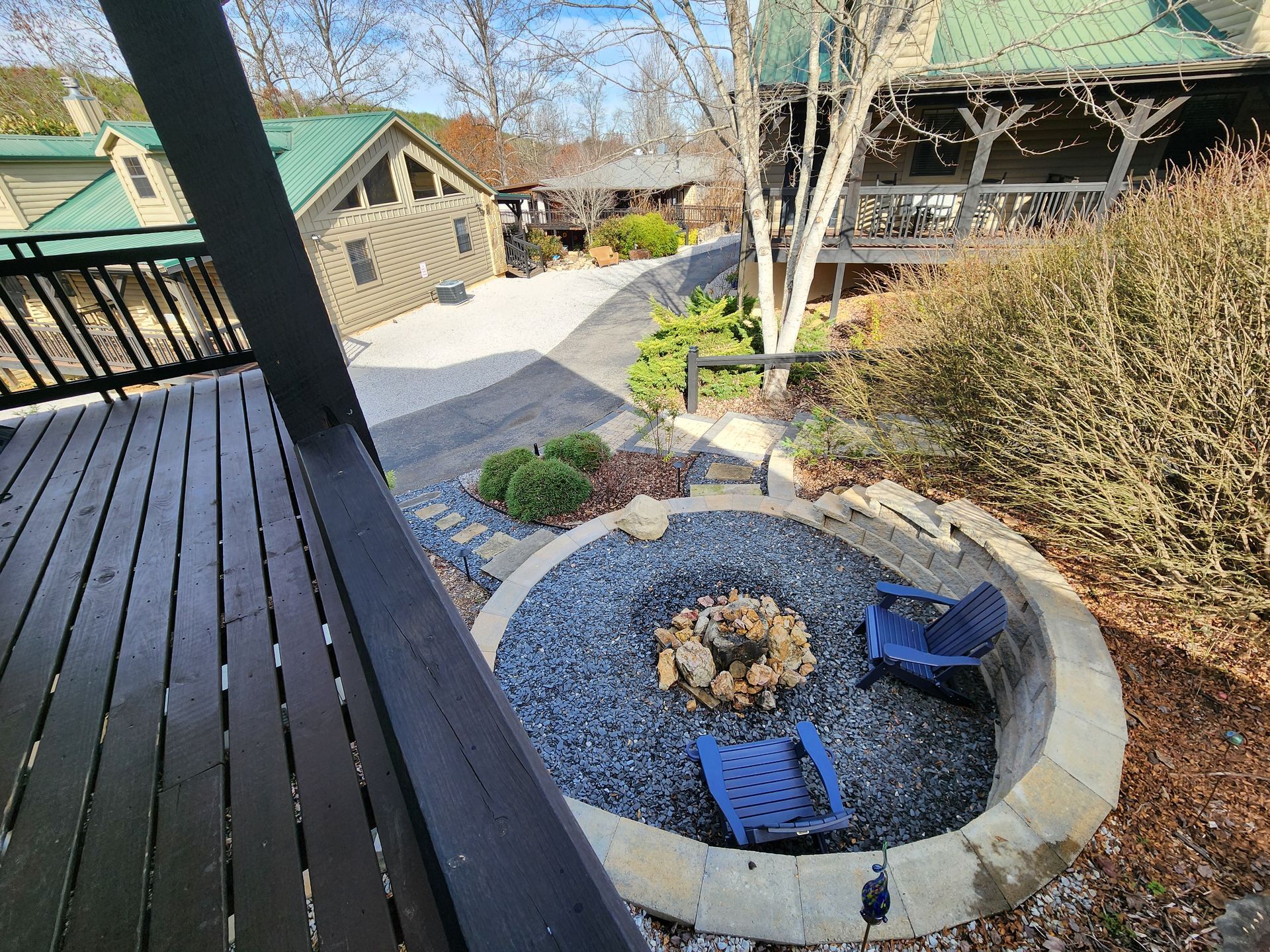 Stone fire pit with two blue chairs, surrounded by gravel, steps, and buildings with green roofs.