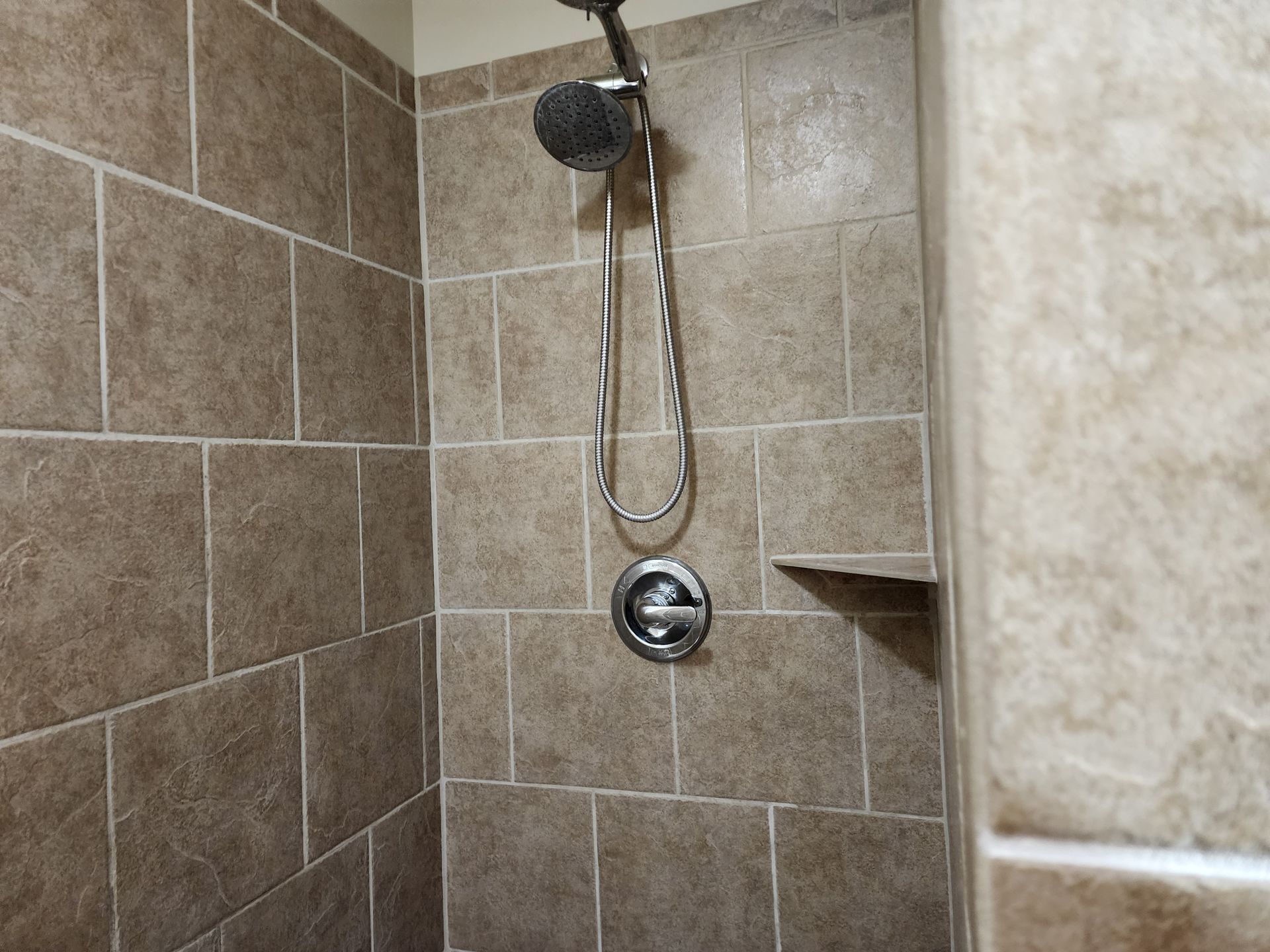 Shower stall with brown tiled walls and silver shower fixtures.