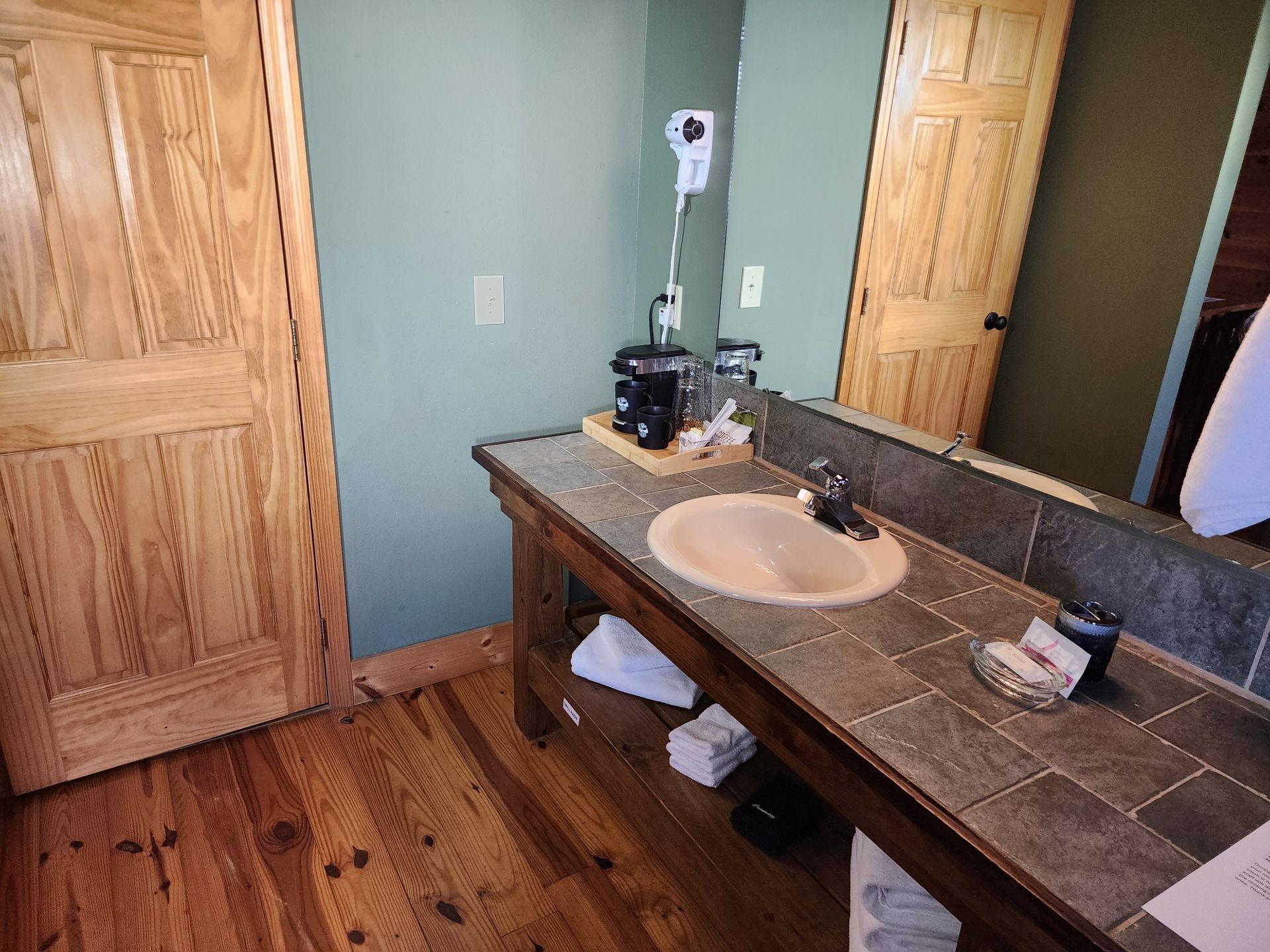 Bathroom with wooden doors and vanity, light green wall, and tile countertop.