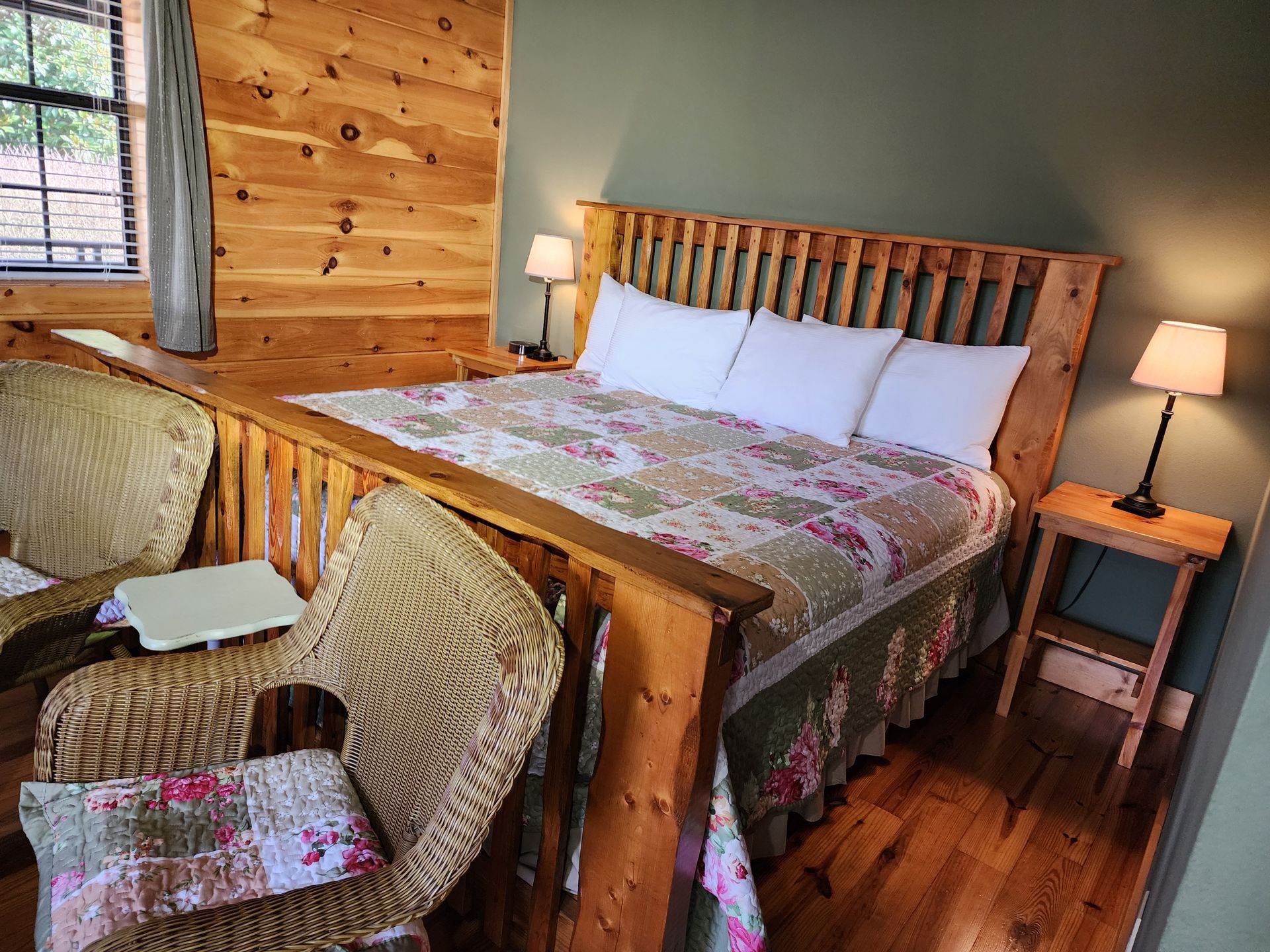 Bedroom with wooden bed frame, floral quilt, wicker chairs, and small side tables with lamps.