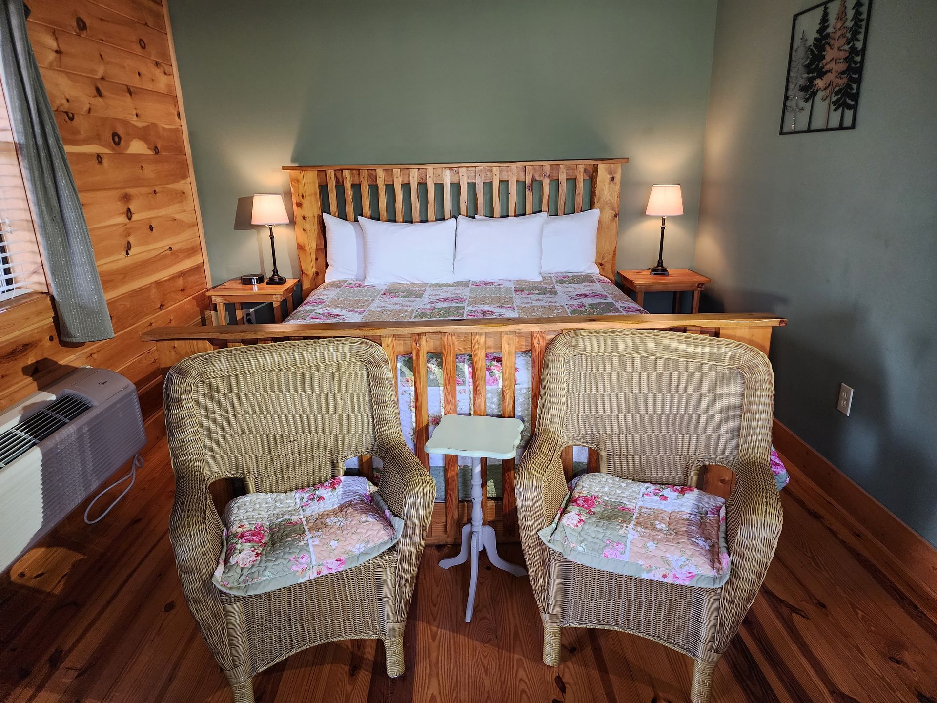 Bedroom with a large wooden bed, two wicker chairs, small table, lamps, and a window.