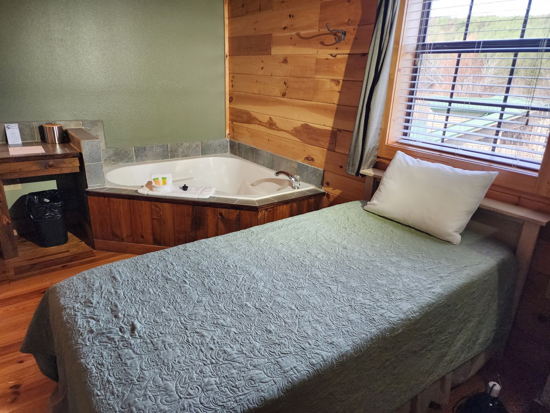 Cozy cabin bedroom with a spa tub, massage table, and small window. Wood paneling and neutral tones.