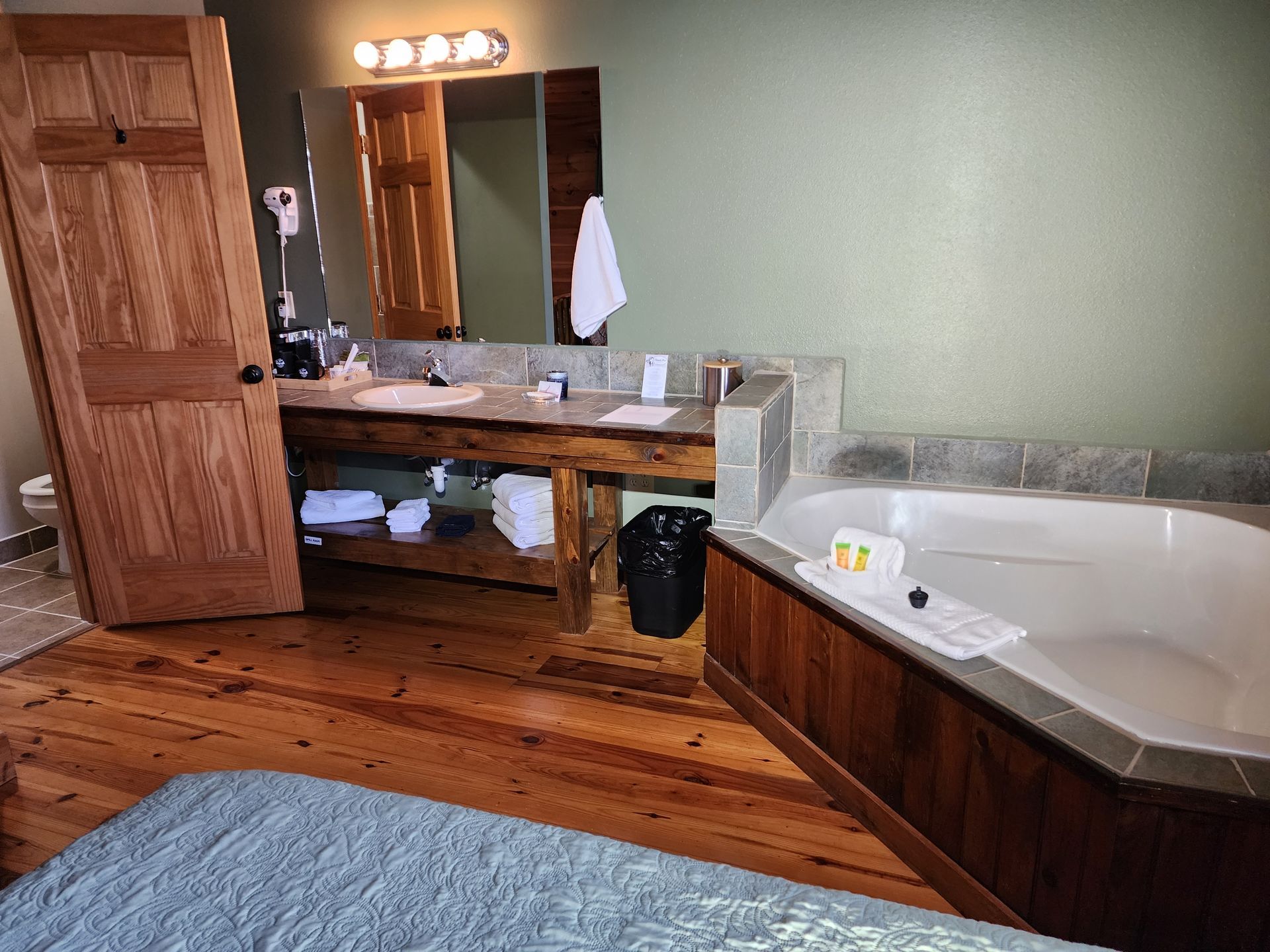 Bathroom with wooden vanity, tub, and hardwood floor. Door is ajar.