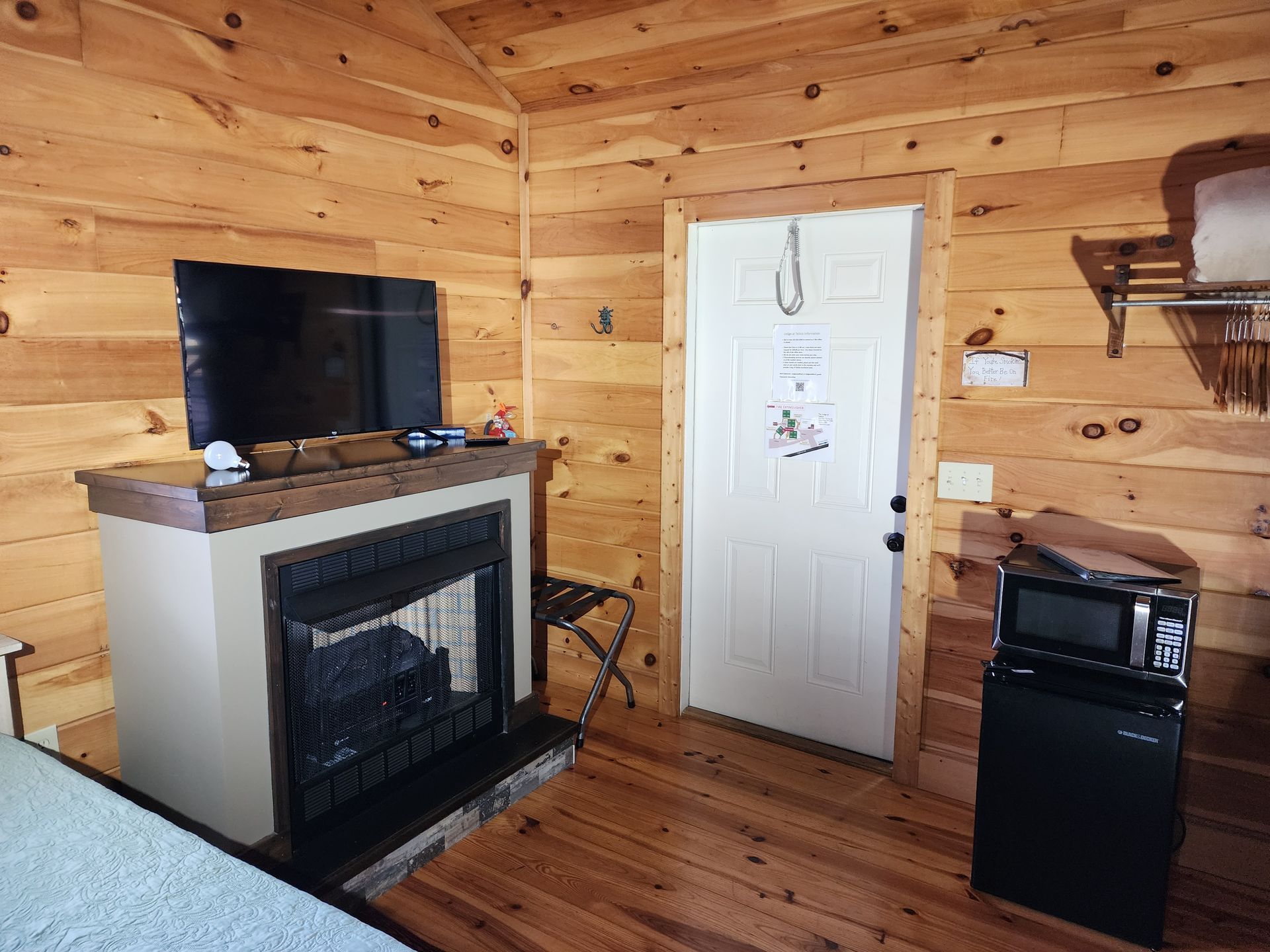 Cozy cabin interior: fireplace with TV, a white door, mini-fridge, wood panel walls, and flooring.