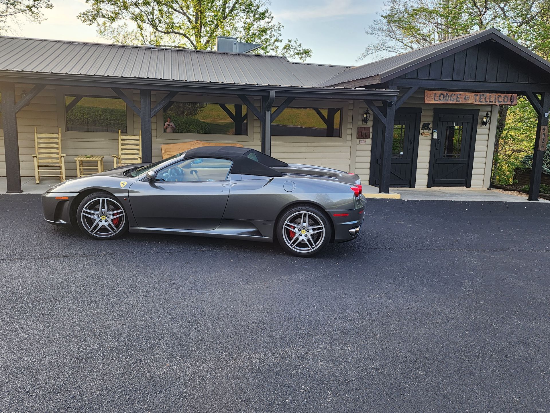 A gray Ferrari convertible parked in front of a rustic building with black trim.