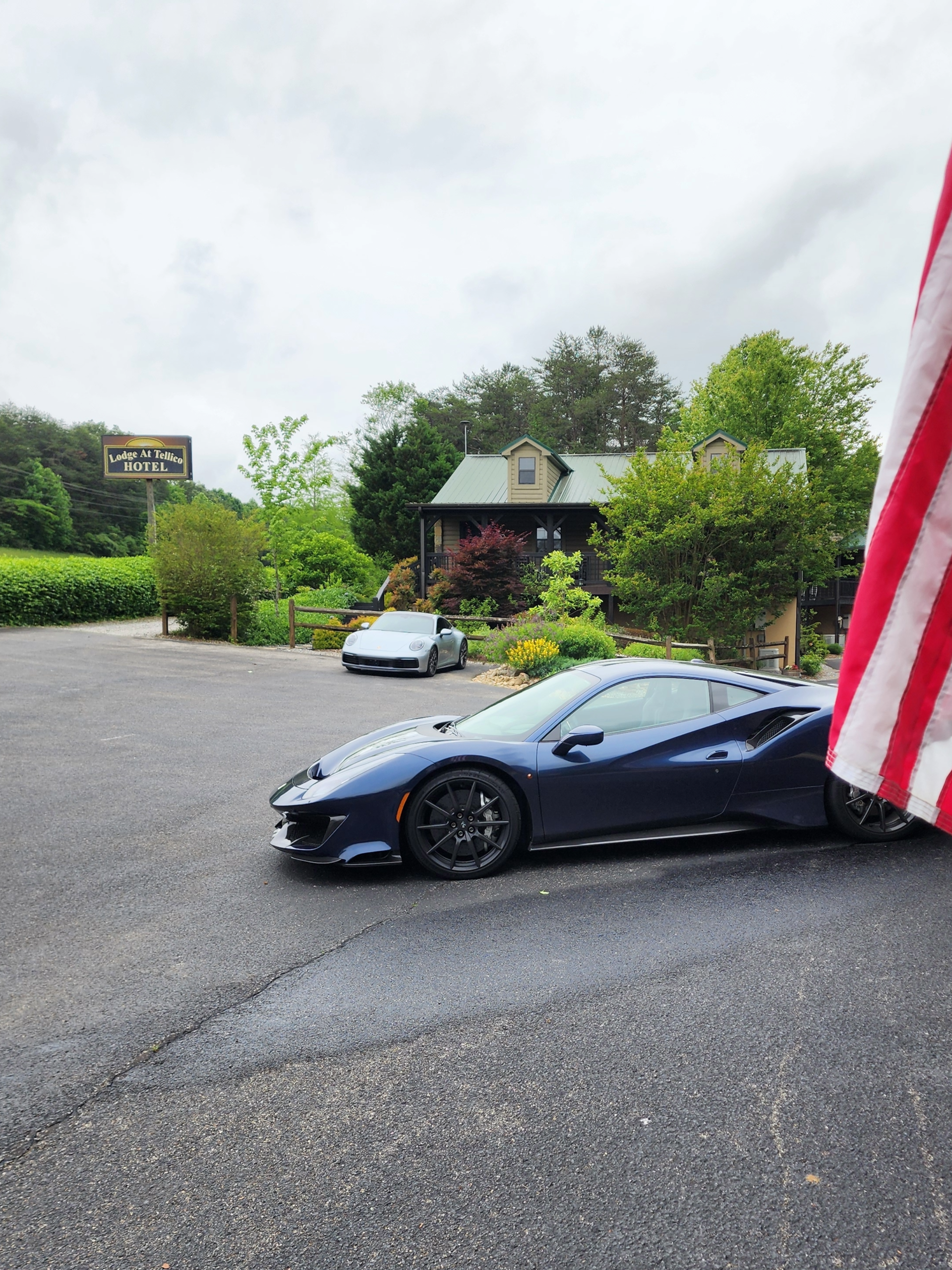 Blue Ferrari sports car parked on asphalt, small building in background, overcast day.