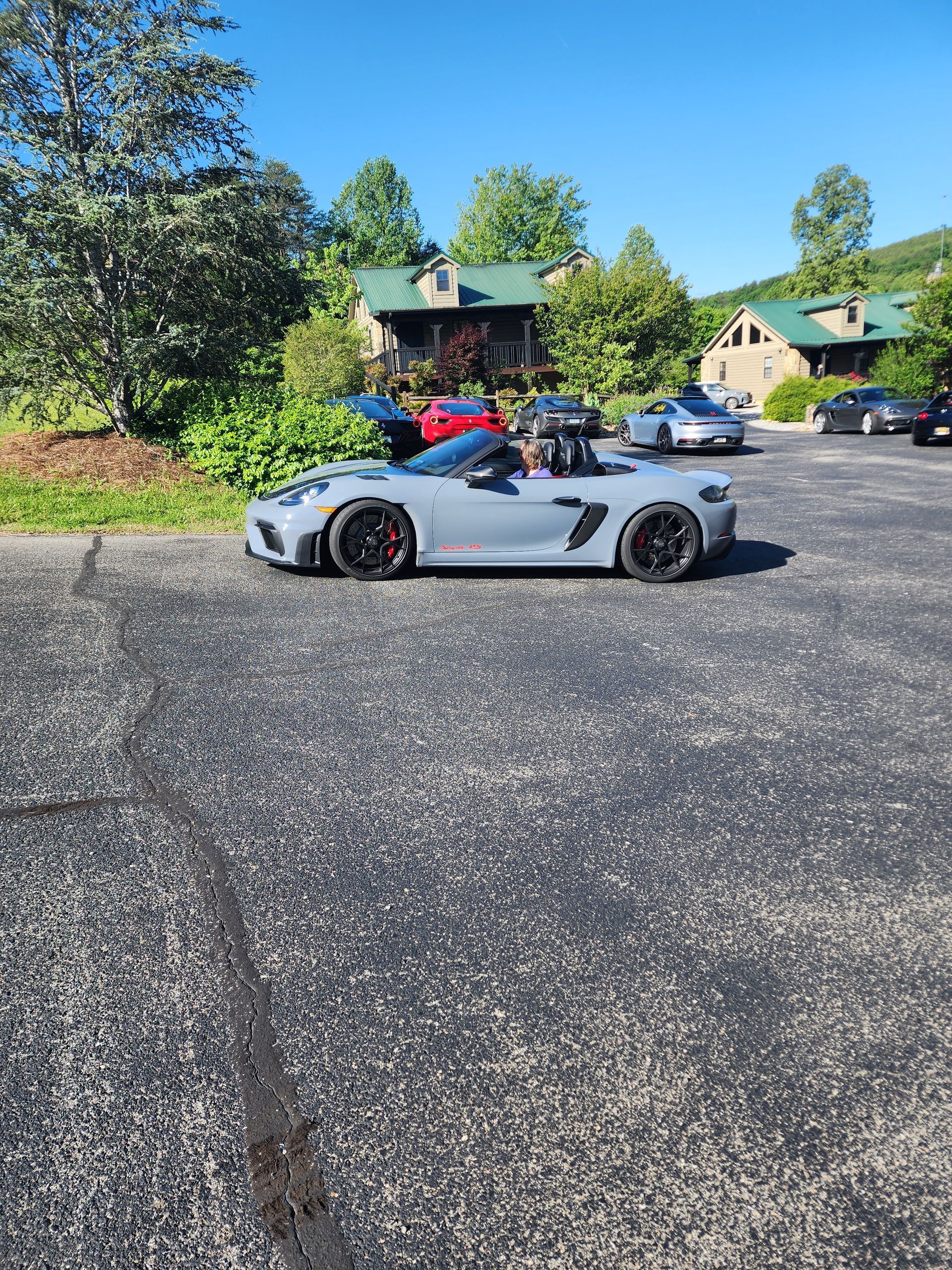 Gray convertible sports car parked in lot with buildings and trees.