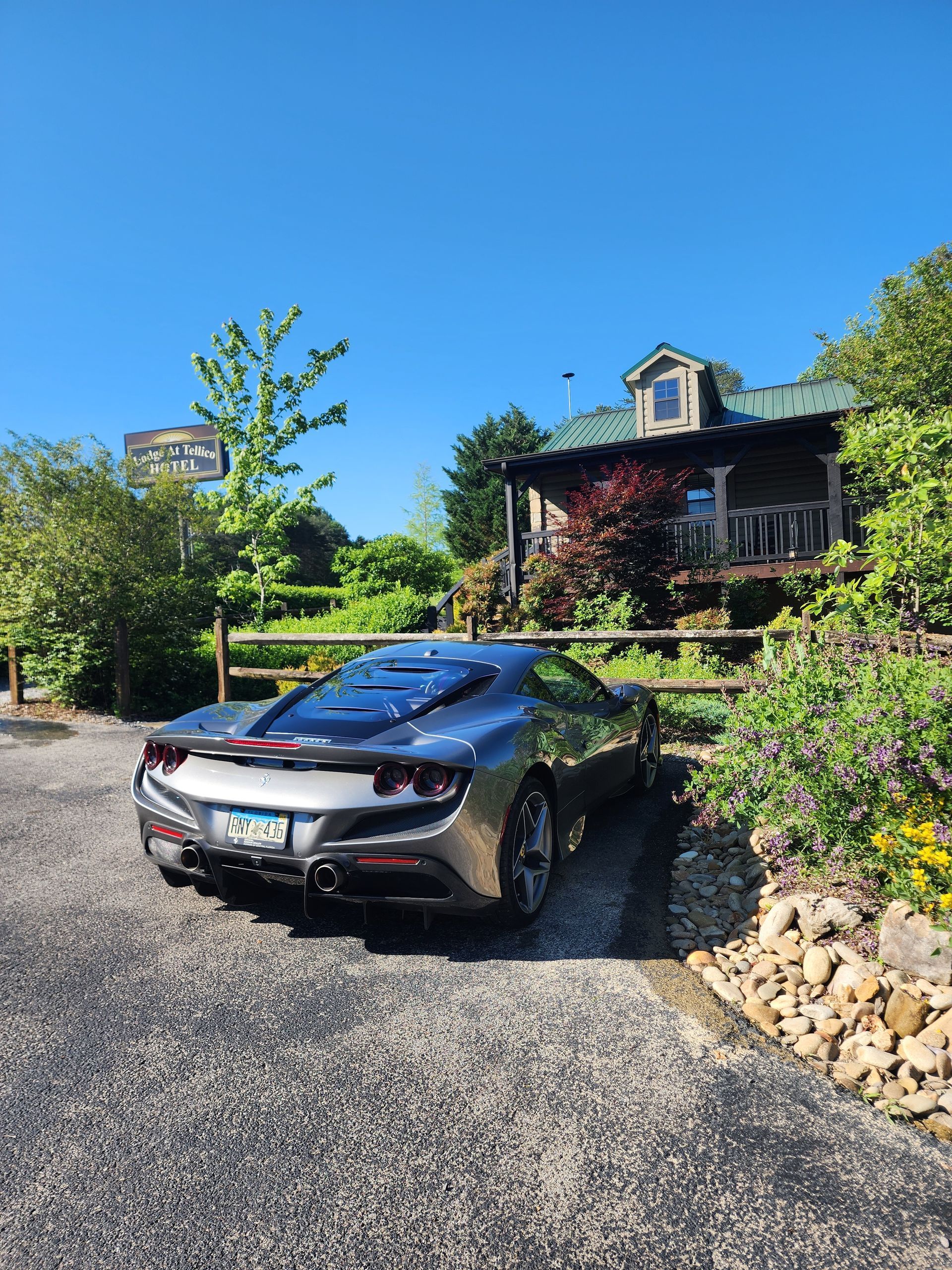 Silver sports car parked in front of a rustic cabin, gravel driveway, clear blue sky.
