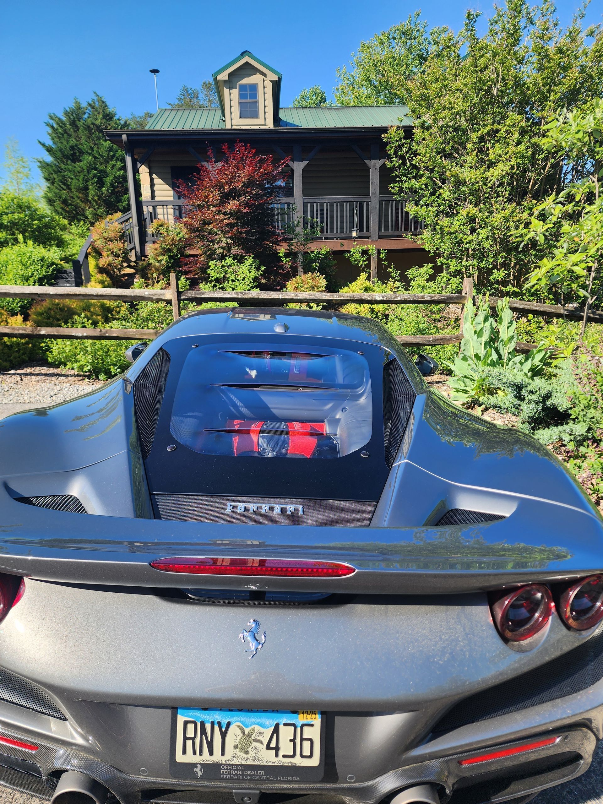 Gray Ferrari parked in front of a rustic cabin, a mountain scene with blue sky.