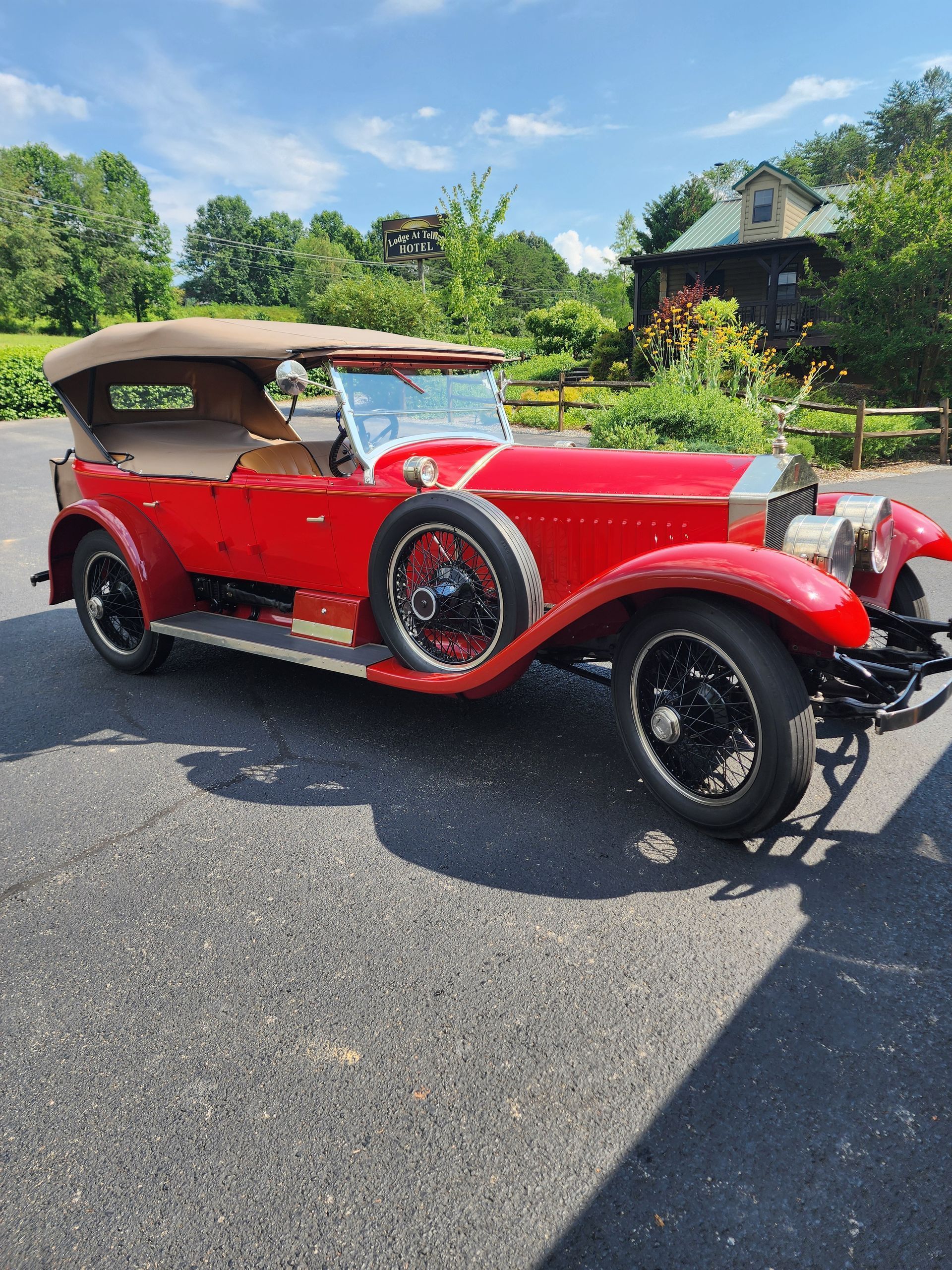 Red vintage car with tan top parked on asphalt on a sunny day.