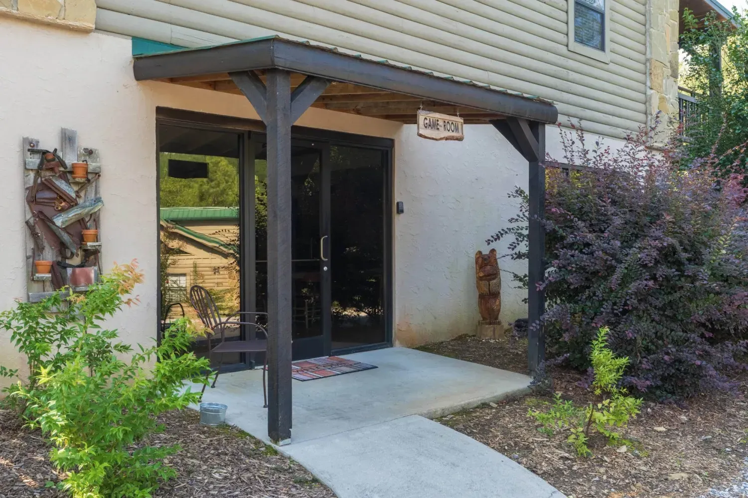 Entrance to a business with dark framed doors under a wooden awning; landscaping and art.