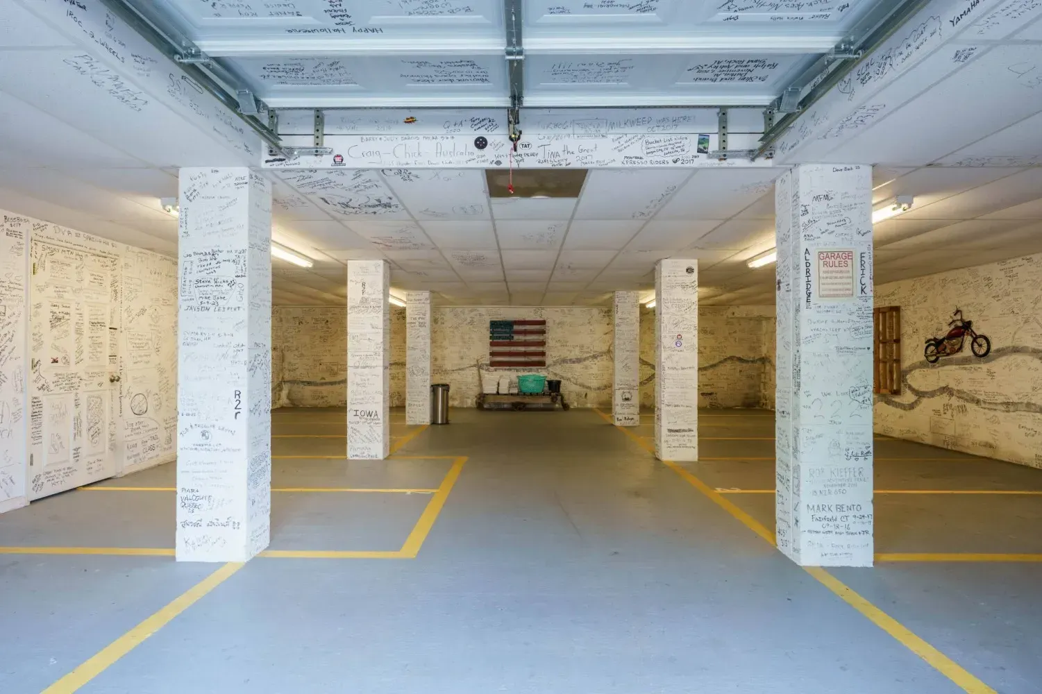 A garage with white pillars and ceiling covered in writing. An American flag hangs at the back.