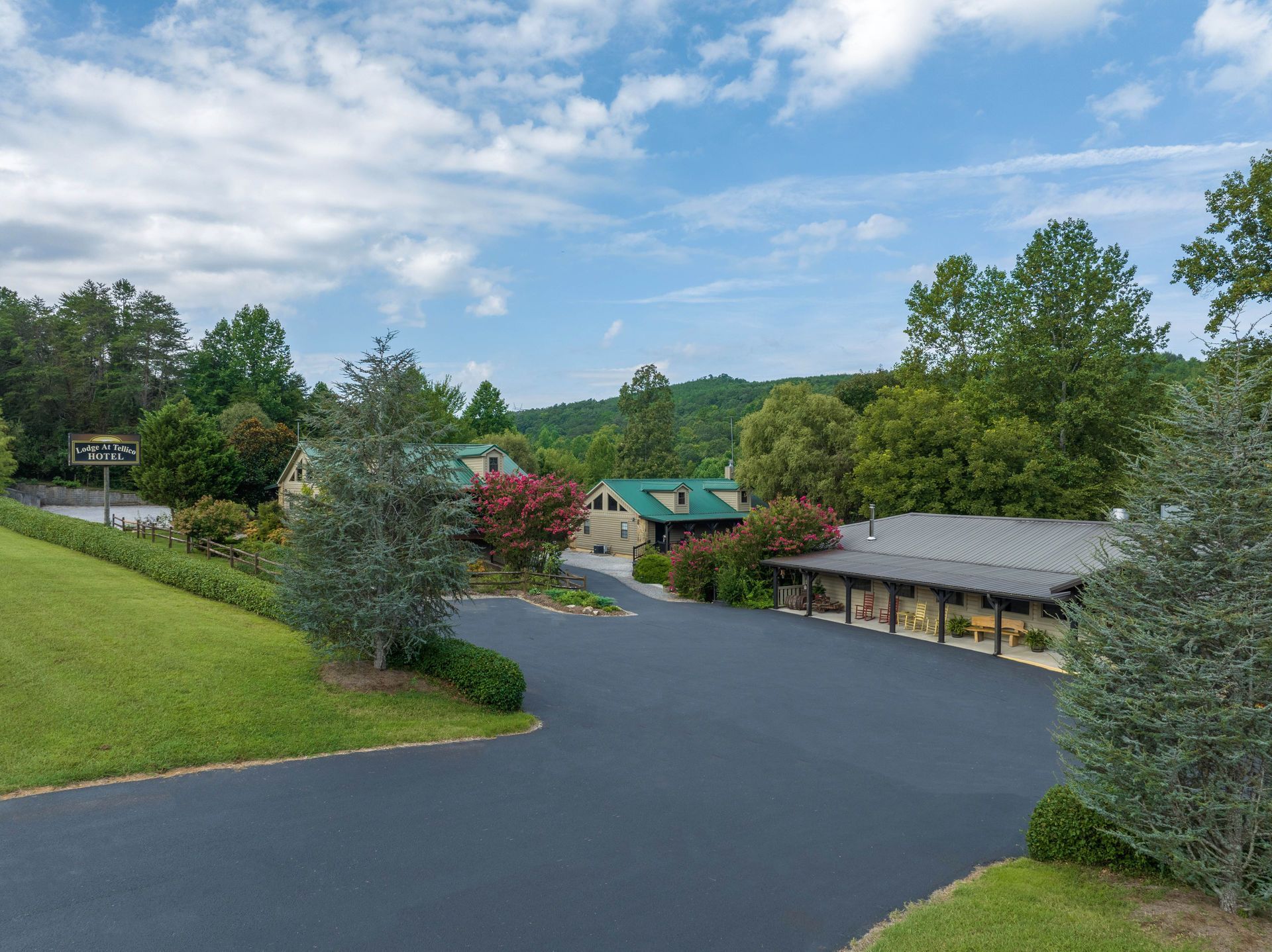 Black asphalt driveway leads to buildings with green roofs, surrounded by trees and greenery.