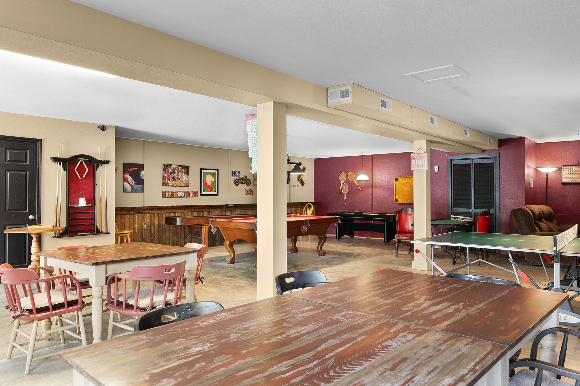 Recreation room with pool tables, a ping pong table, tables, and seating. Beige and red walls, beige ceiling.