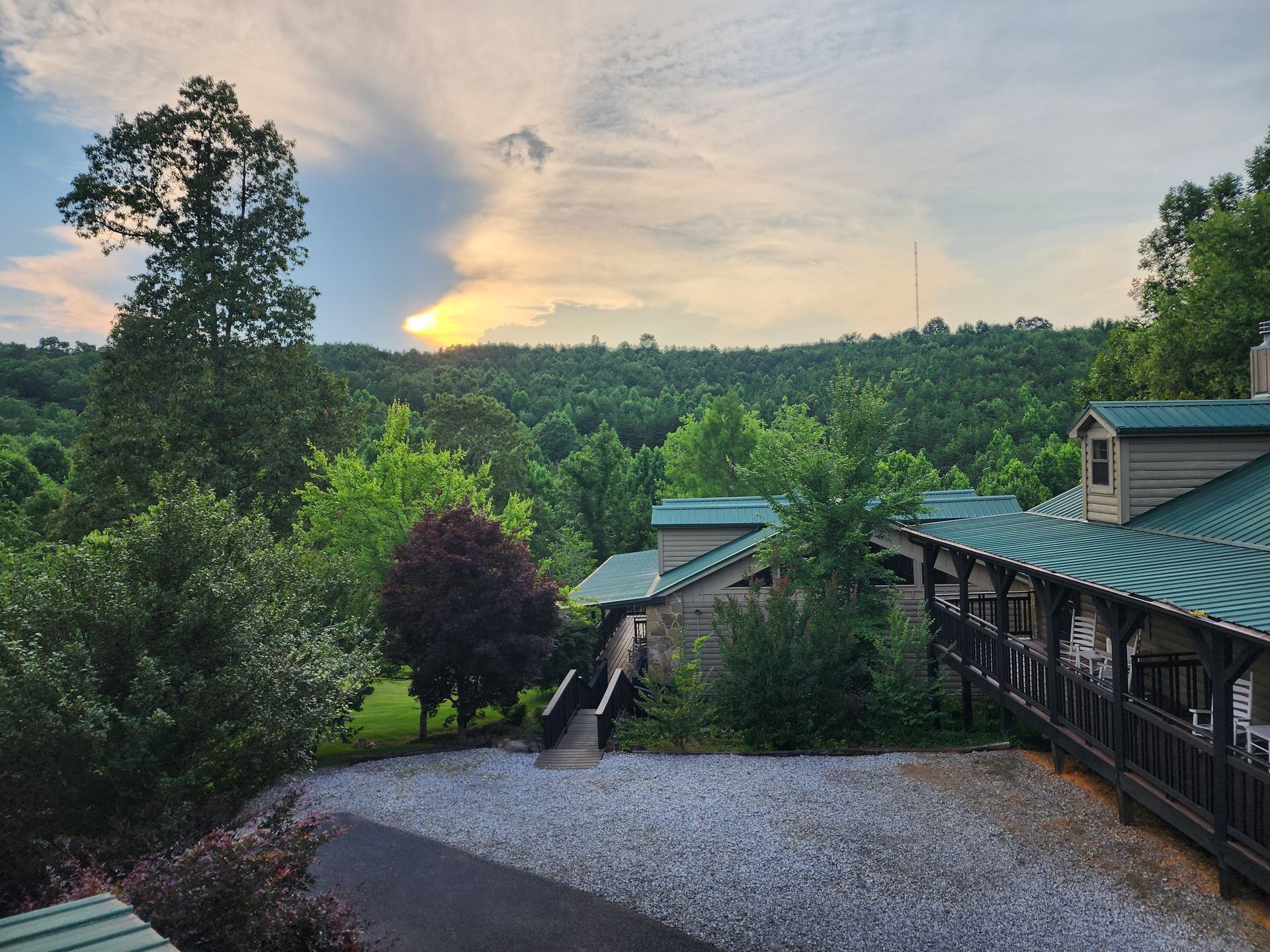 Sunset over forested hills, buildings with green roofs in the foreground.