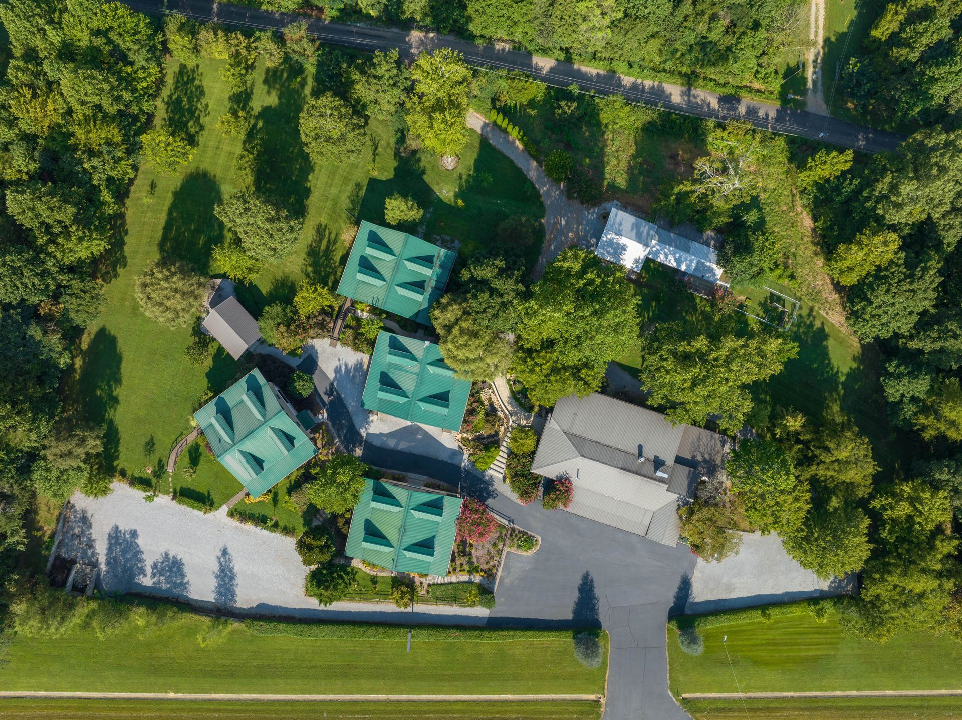 Aerial view of several green-roofed buildings surrounded by trees and a paved driveway.