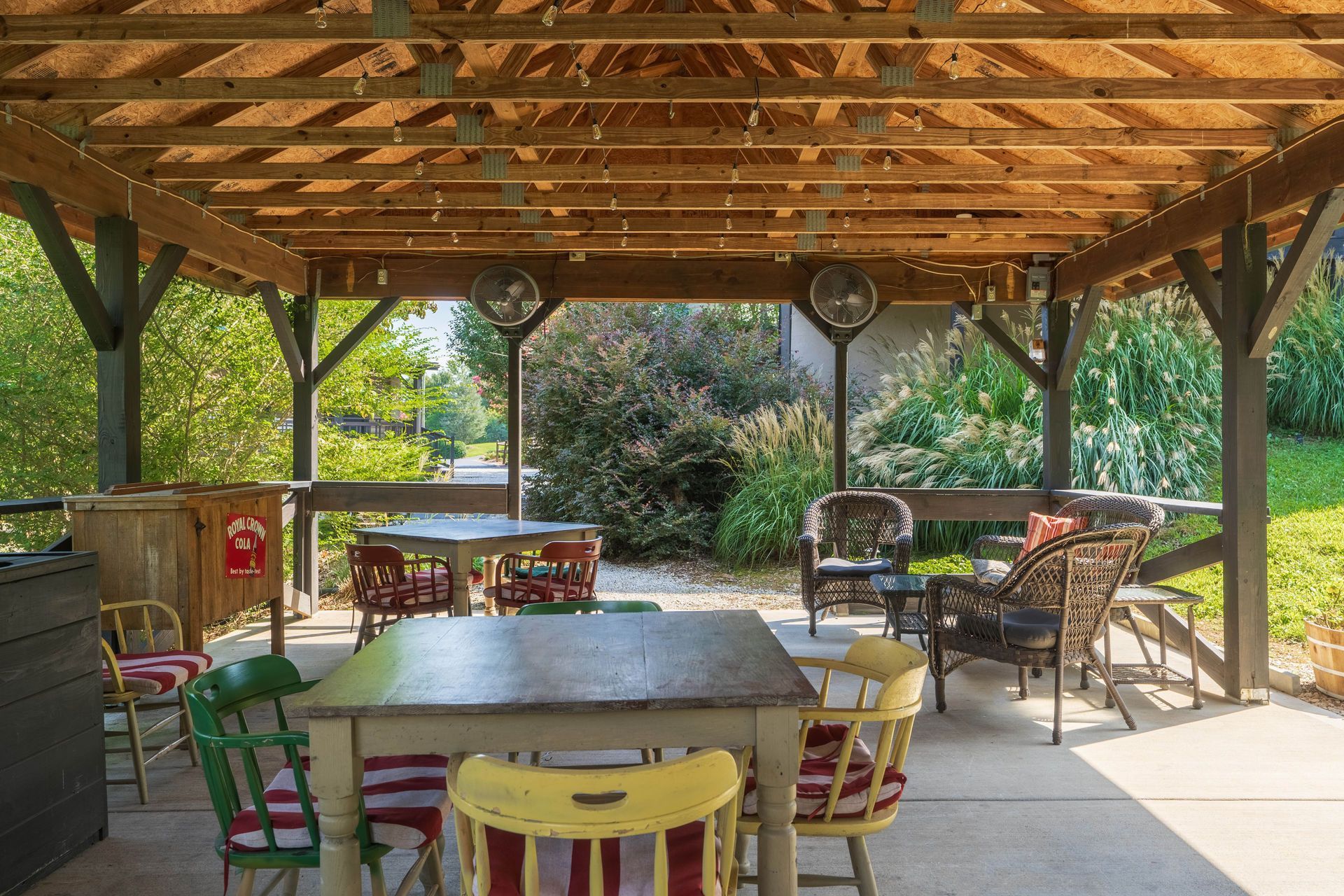 Covered outdoor seating area with tables and chairs. Fans and string lights hang above.