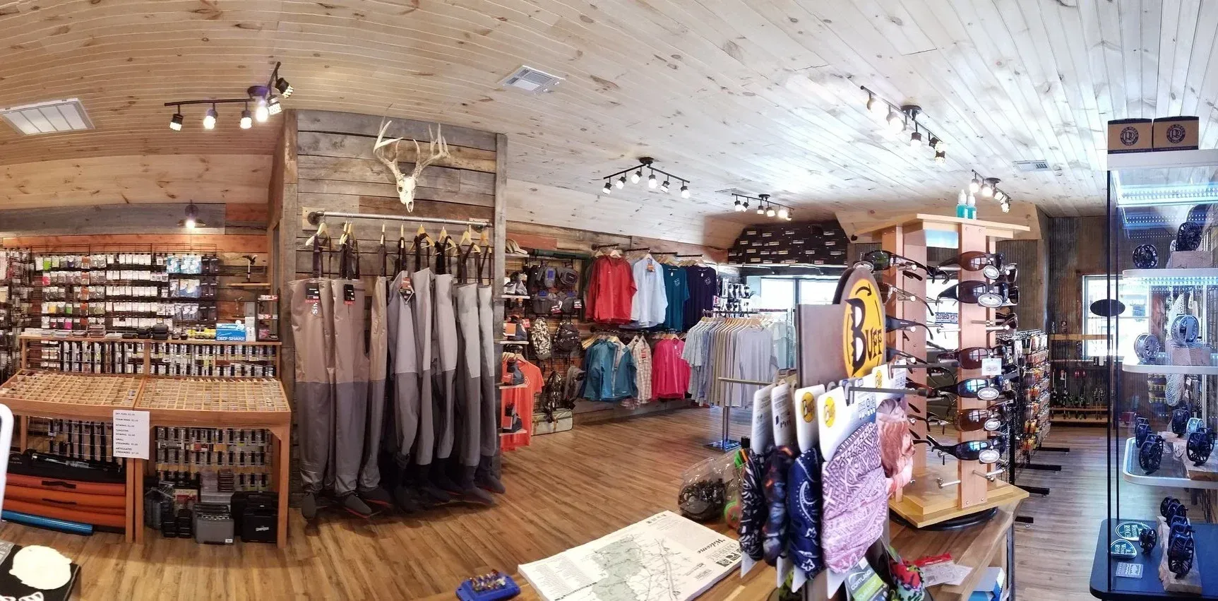Interior of a fishing supply store with wooden floors, displays of clothing and gear, and overhead lighting.