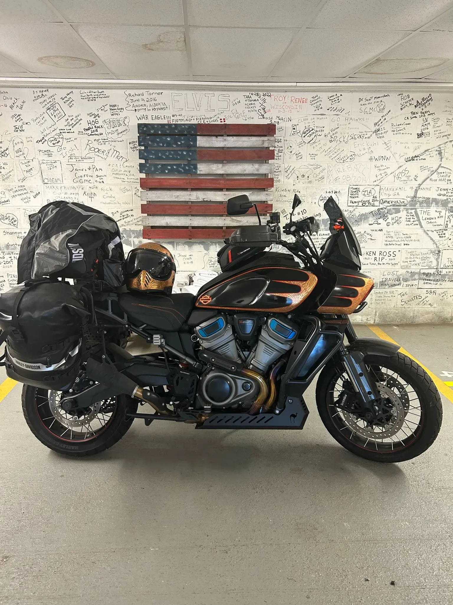 Motorcycle parked in front of a rustic American flag. Black motorcycle with luggage.