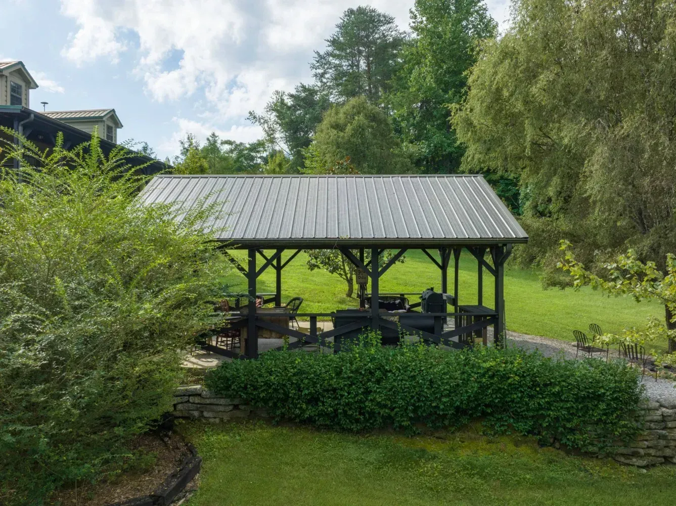 Wooden gazebo with a metal roof in a grassy area, trees in background.