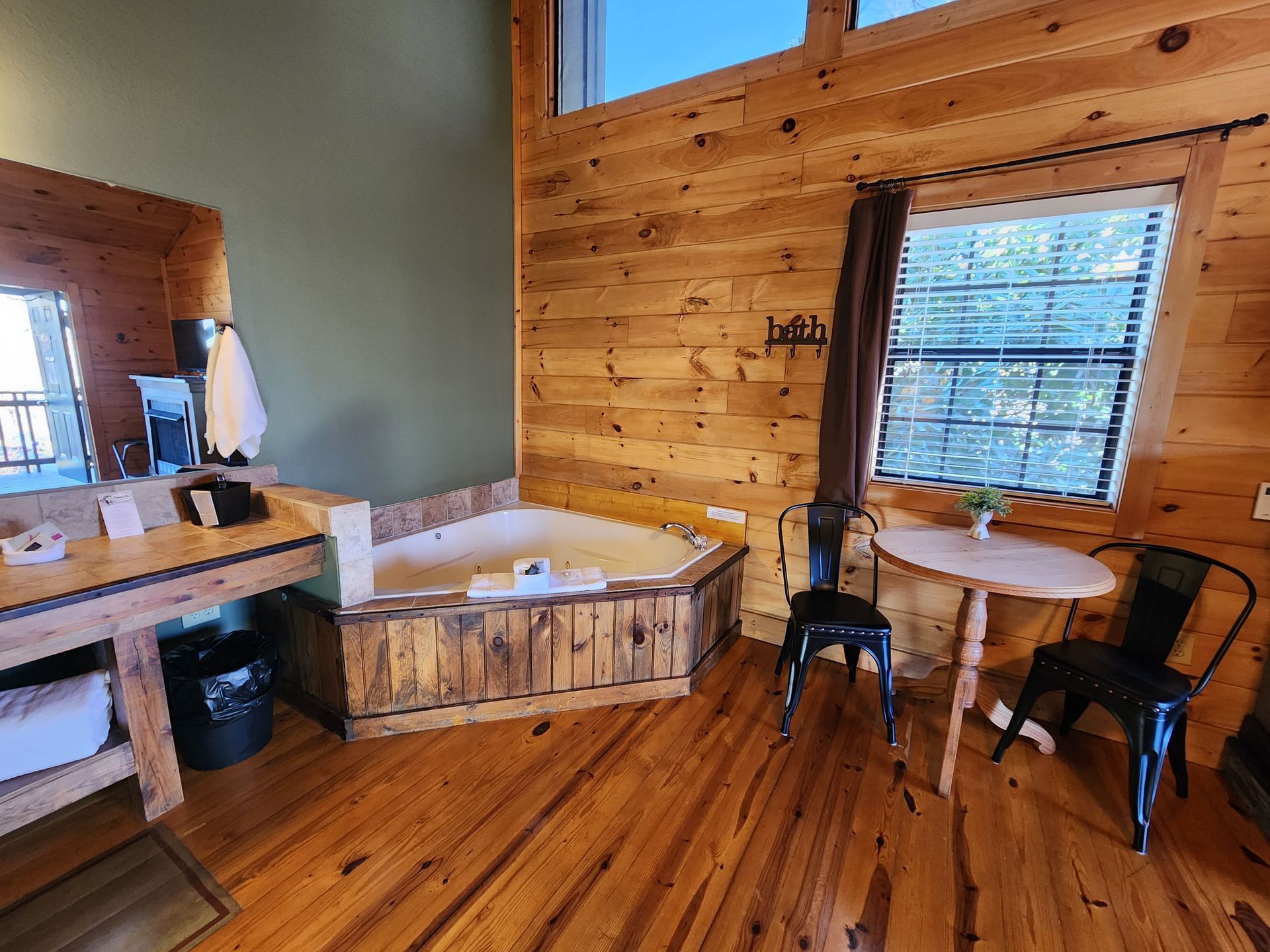 Cozy cabin interior with a jacuzzi, wooden walls, a small table, and chairs.