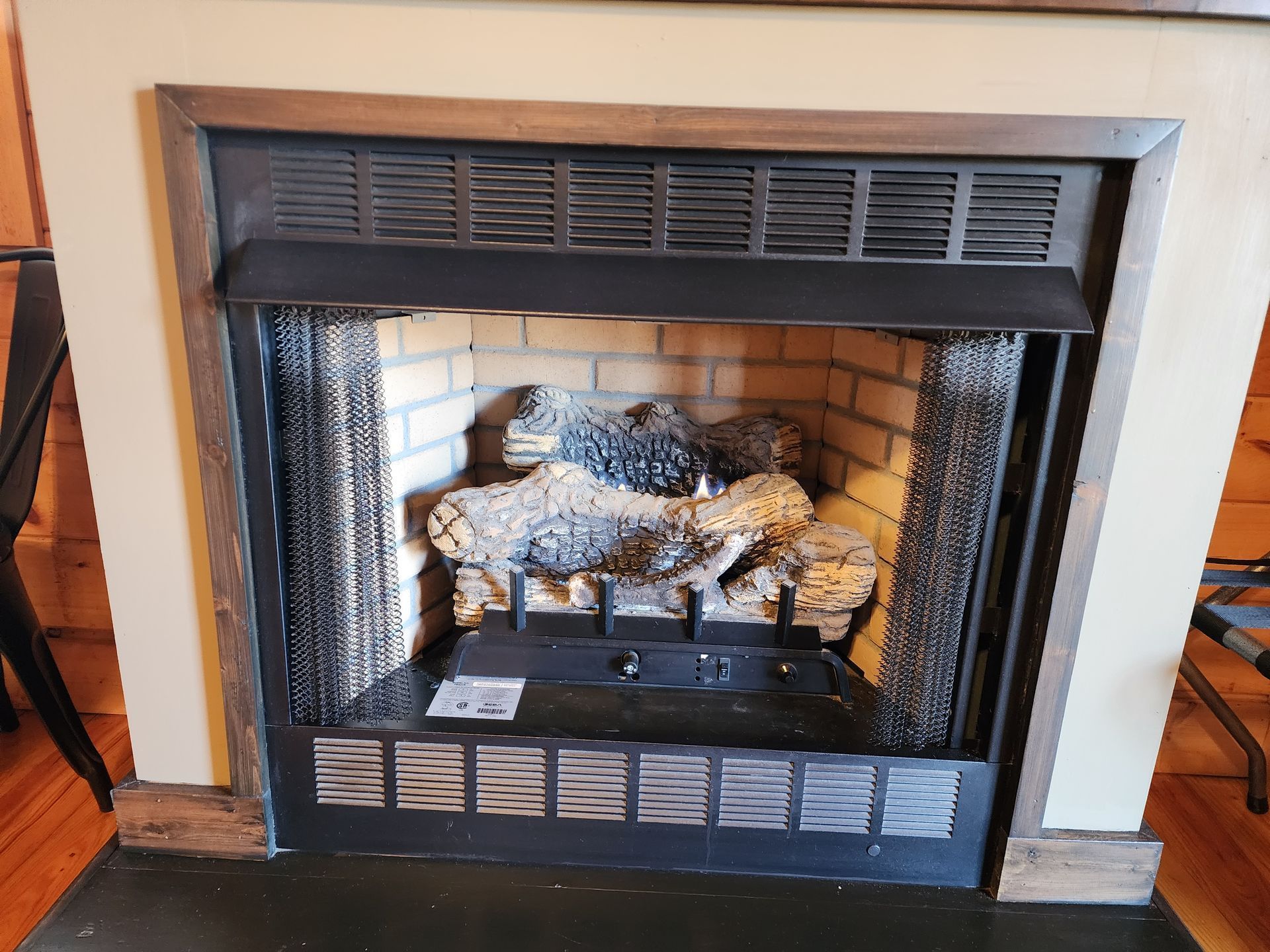 Fireplace with faux logs, black metal screen and trim, tan brick interior.