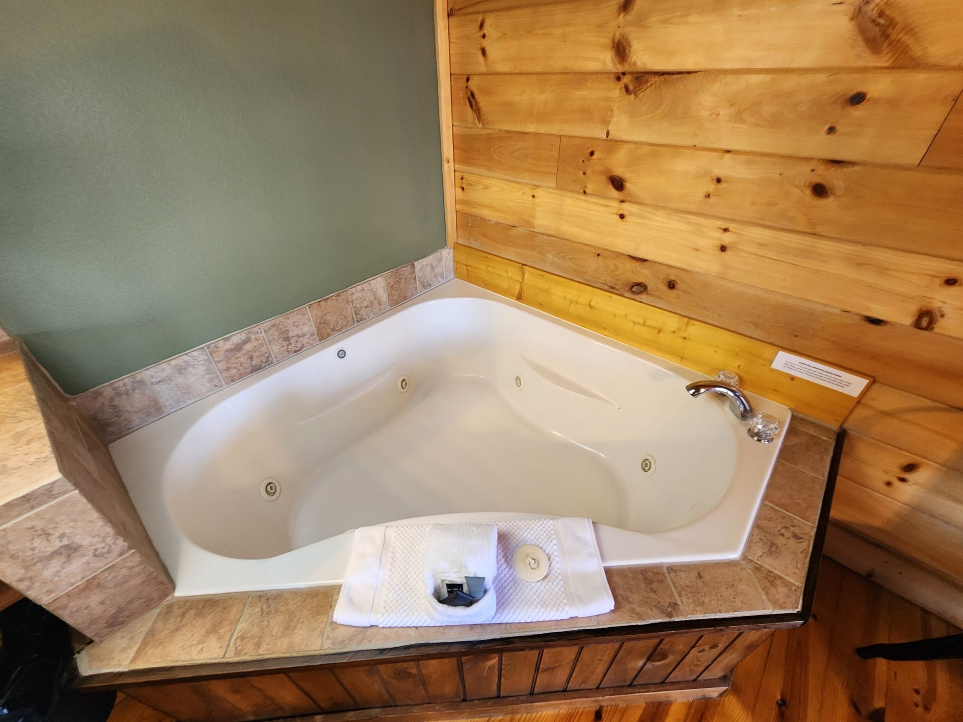 Corner jacuzzi tub surrounded by wood paneling and stone trim in a bathroom setting.