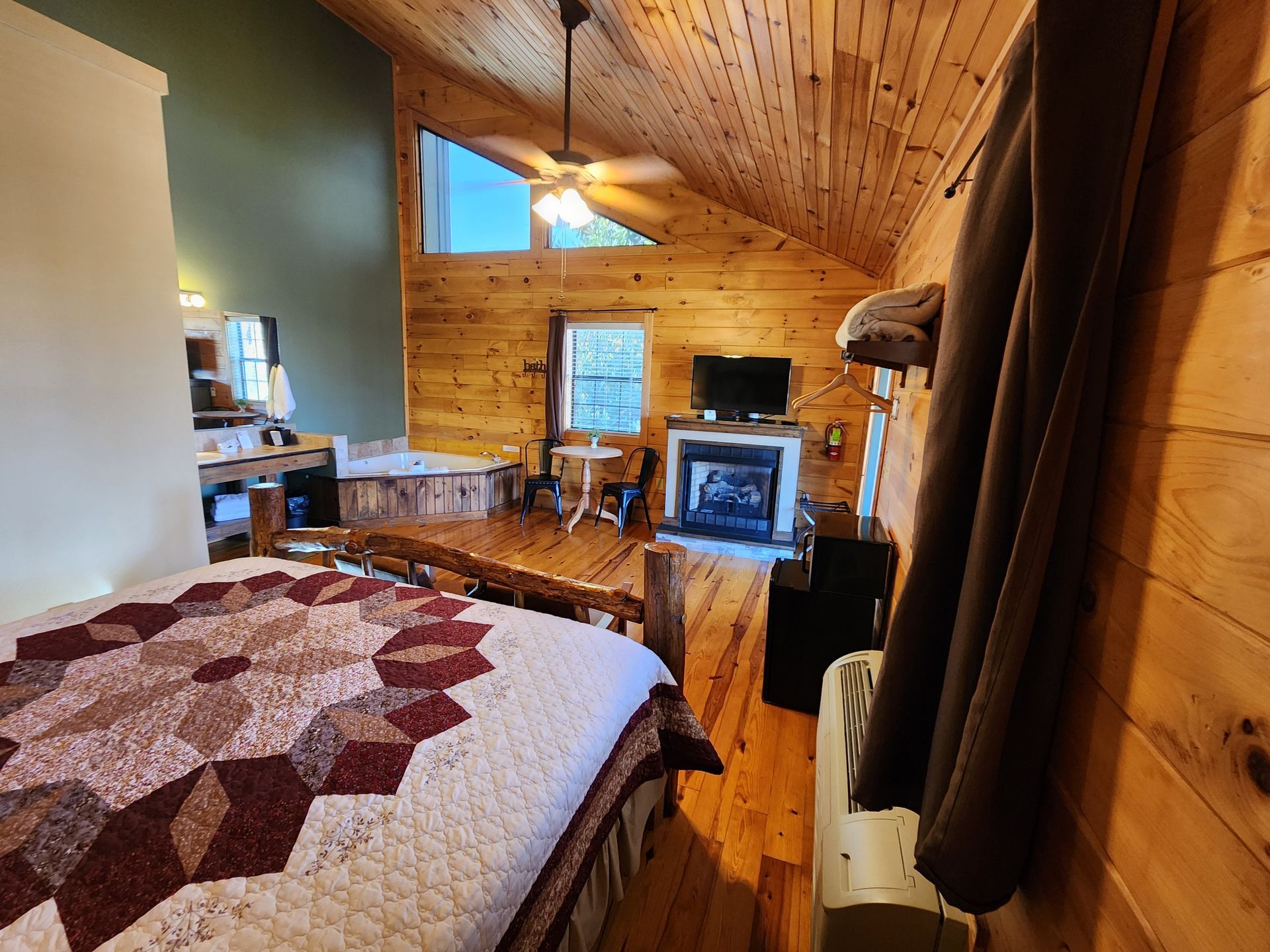 Cozy cabin interior with wooden walls, fireplace, and bed with quilt. A coat hangs on the door.