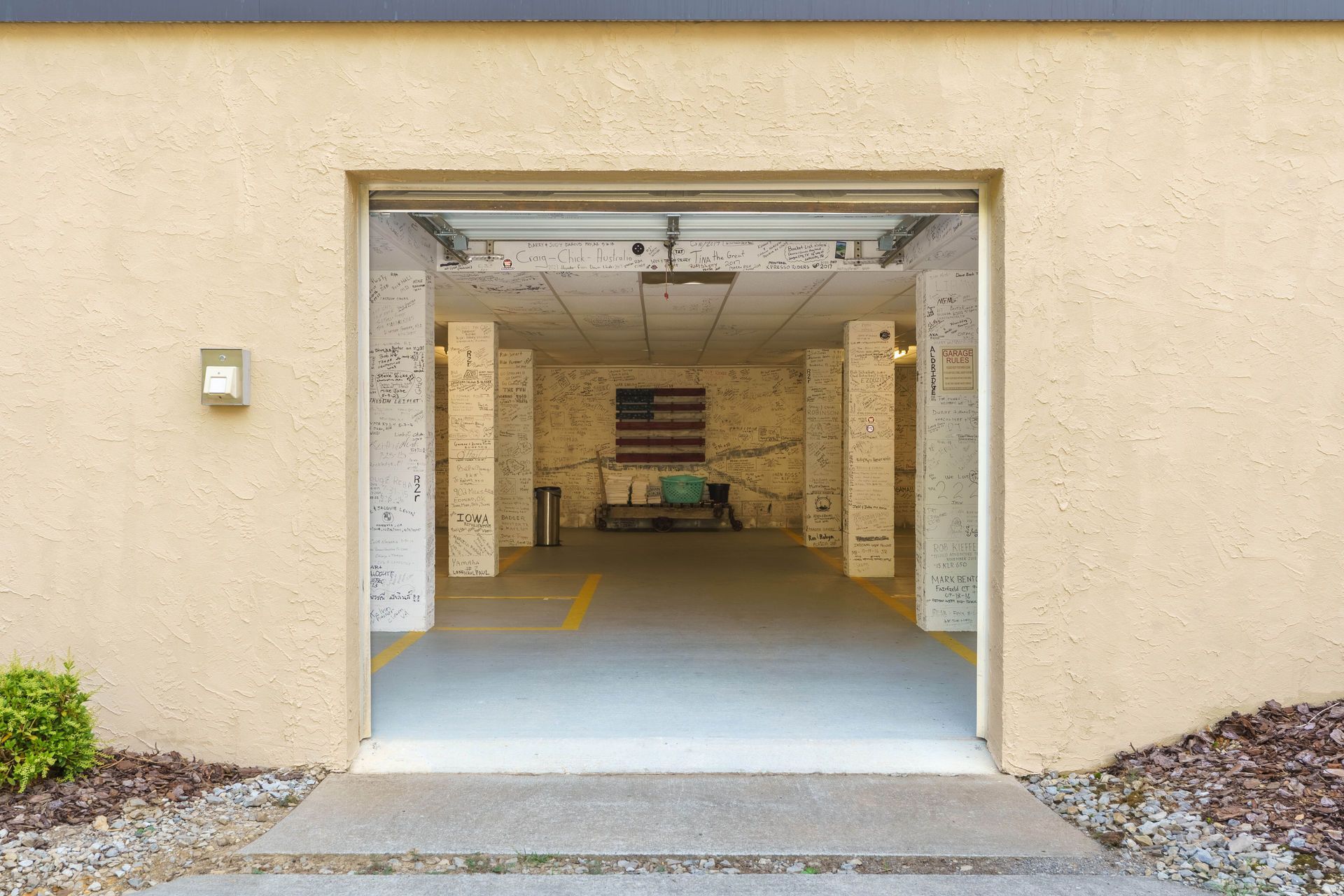Garage entrance with open door, revealing interior with parking spaces and an American flag.