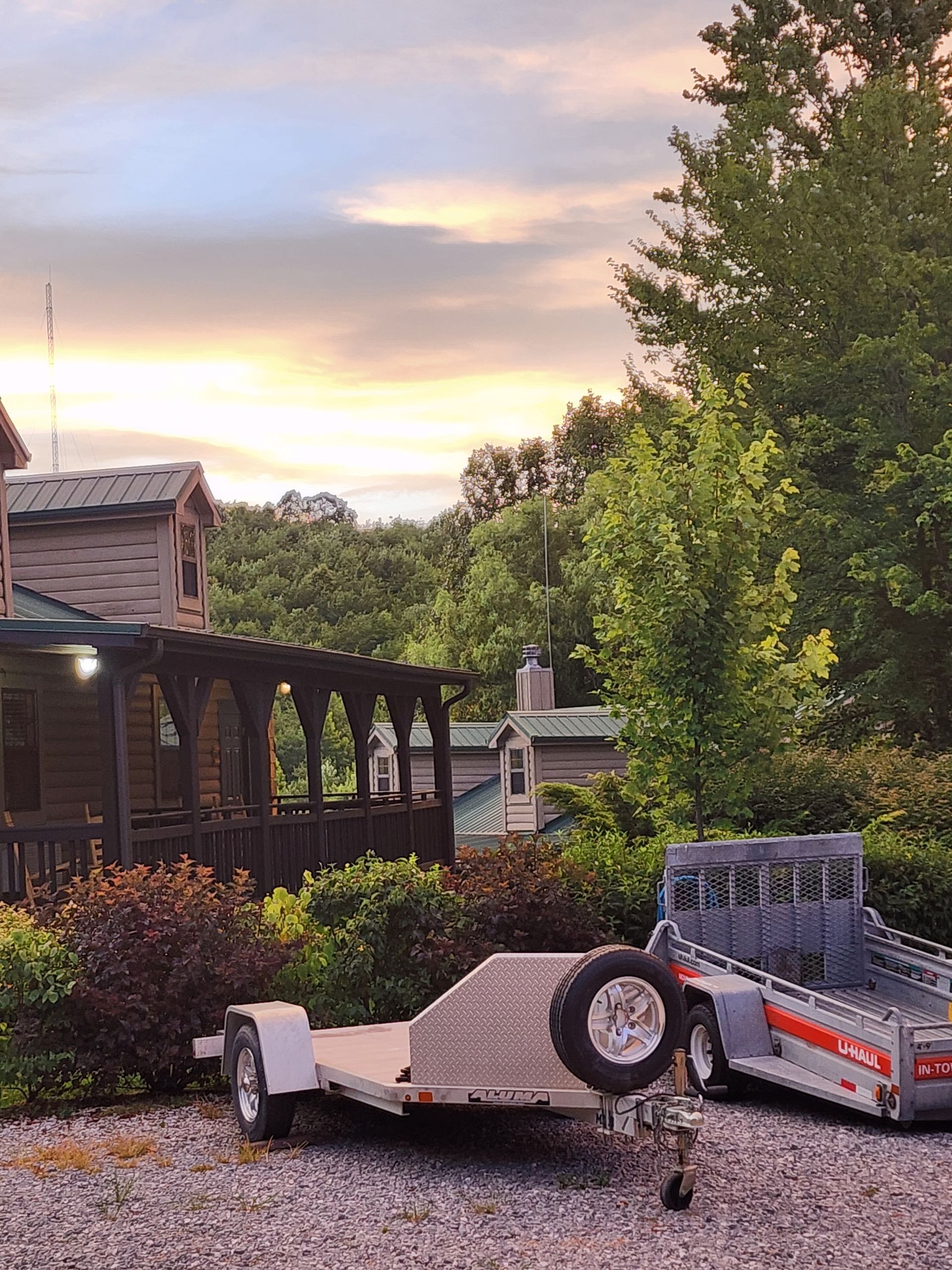 Two trailers parked outside a wooden cabin with green trees under a colorful sky.
