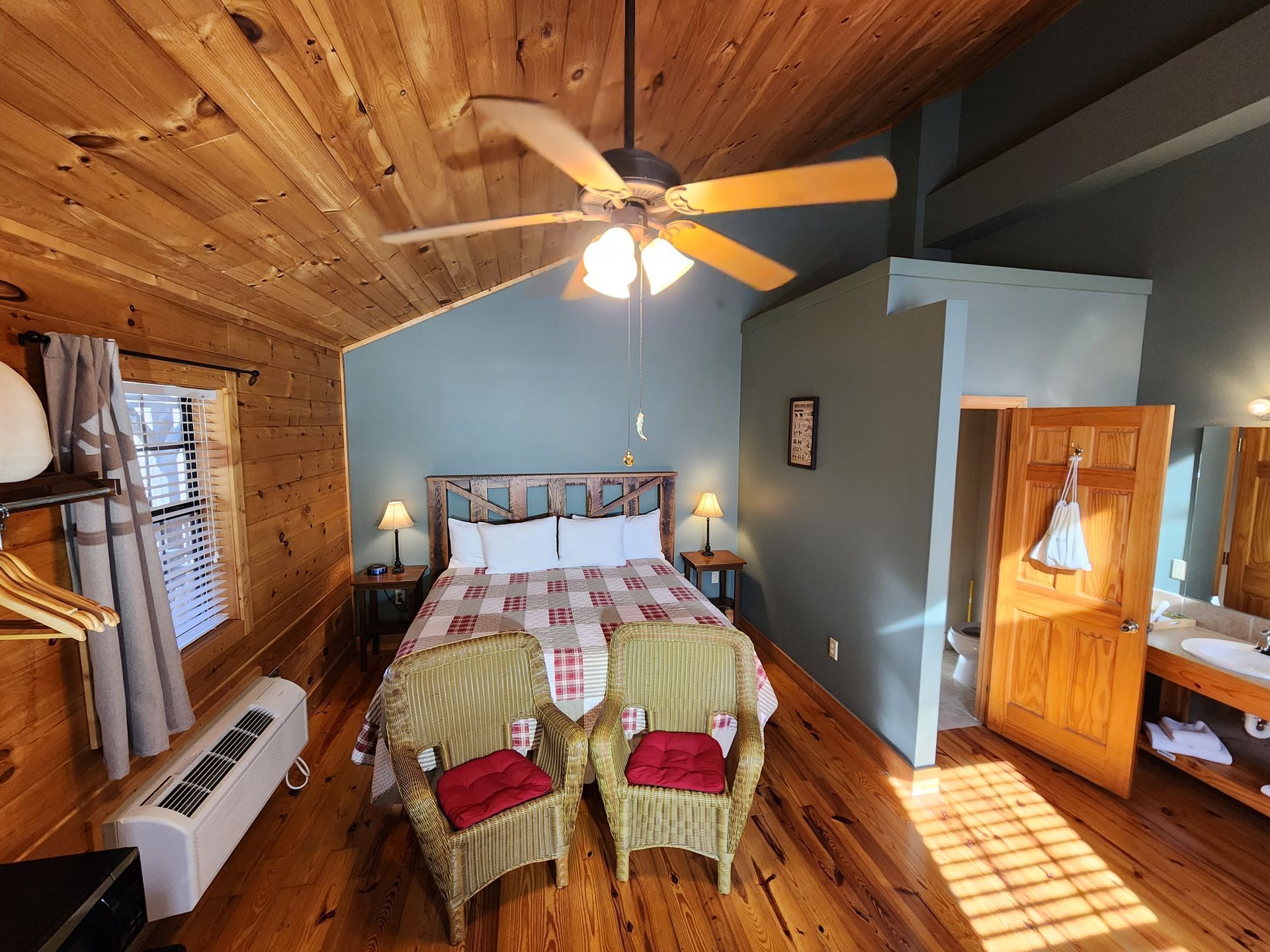 Bedroom with wood paneling, queen bed, two wicker chairs, and a bathroom.