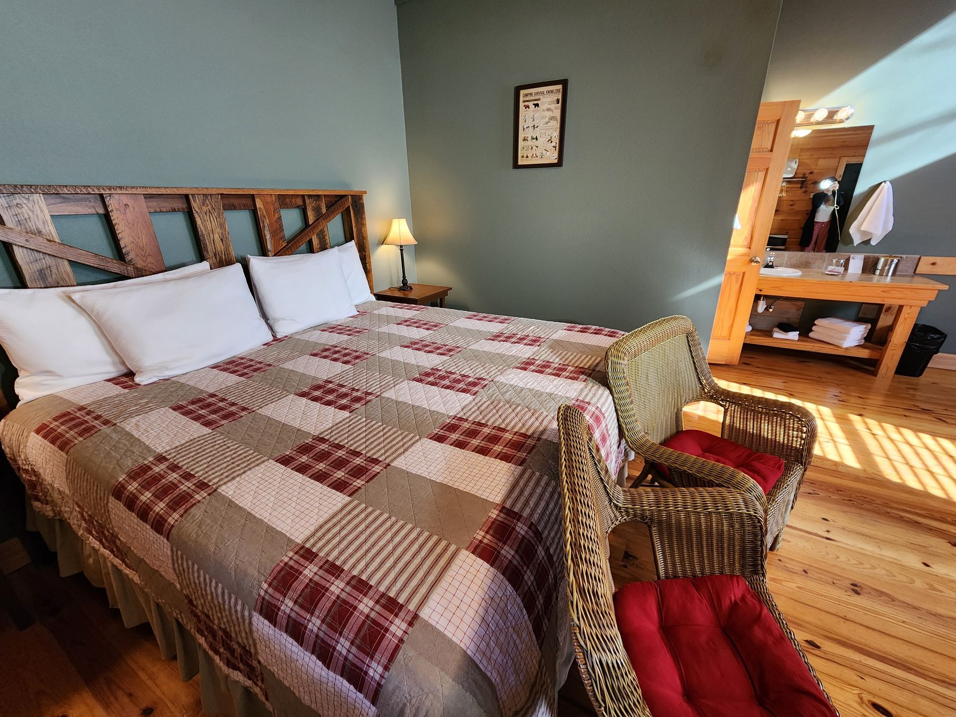 Bedroom with king-sized bed, patchwork quilt, rustic wooden headboard, two wicker chairs, and bathroom.