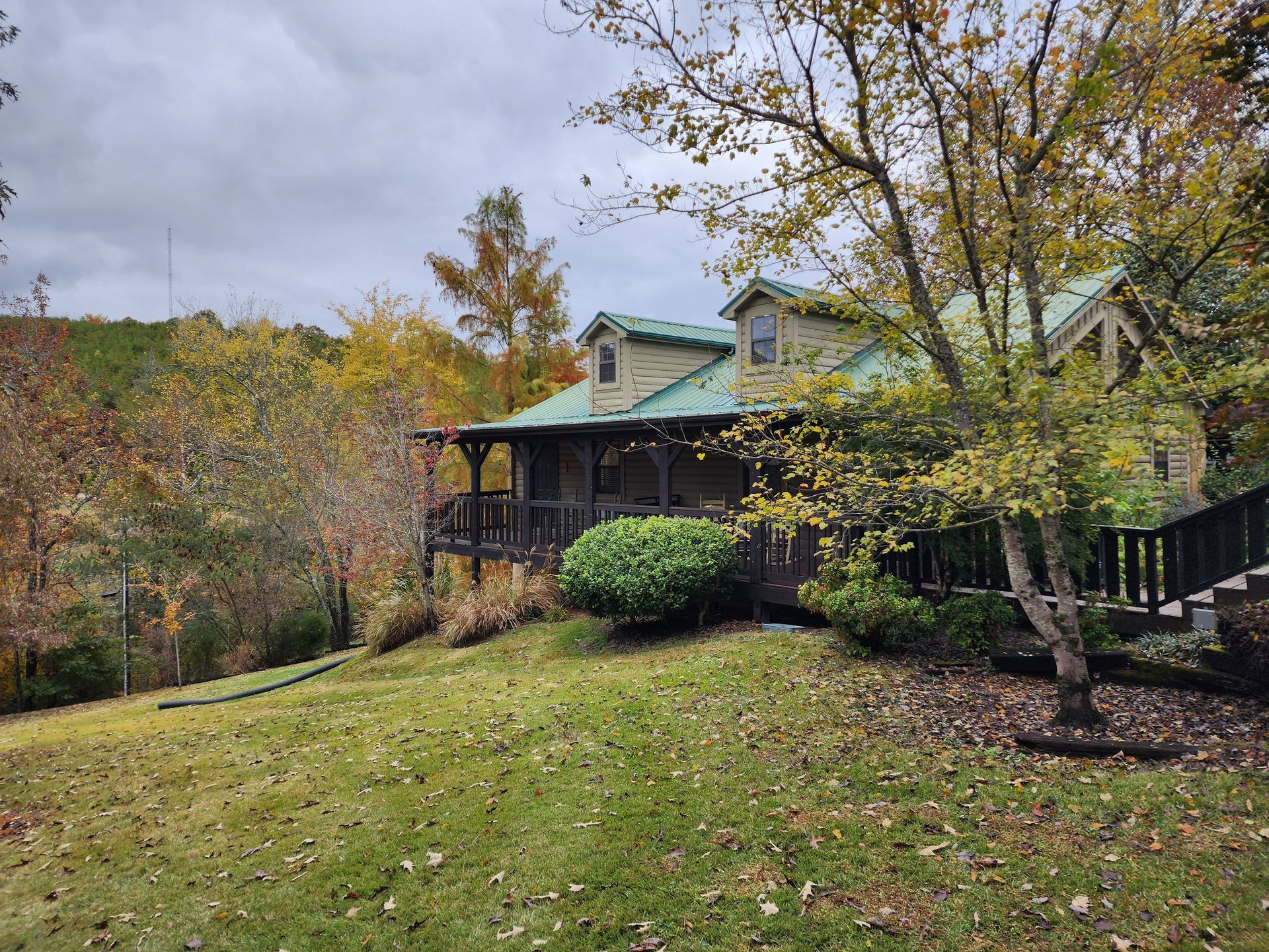 Cabin with green roof and porch, surrounded by autumn trees on a hillside.