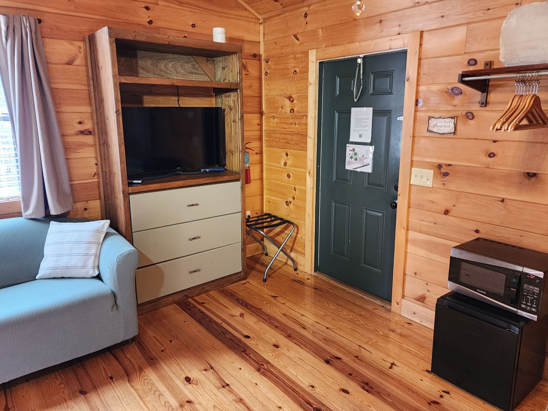 Cozy cabin interior with wood paneling, sofa, TV, dresser, and microwave.