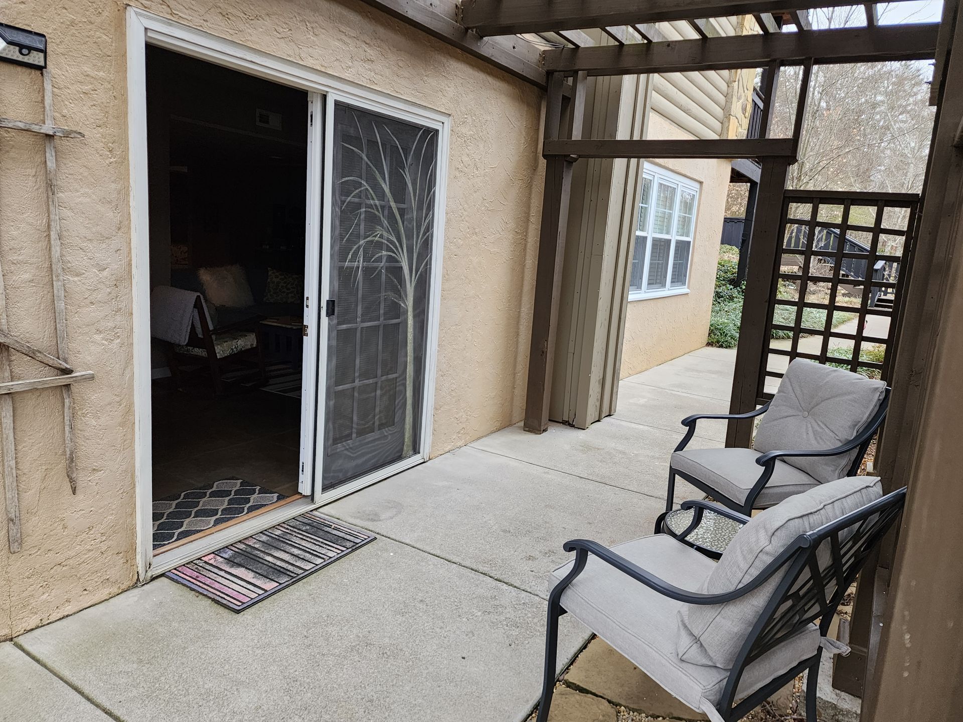 Patio with chairs, sliding door, and trellis; beige stucco exterior.
