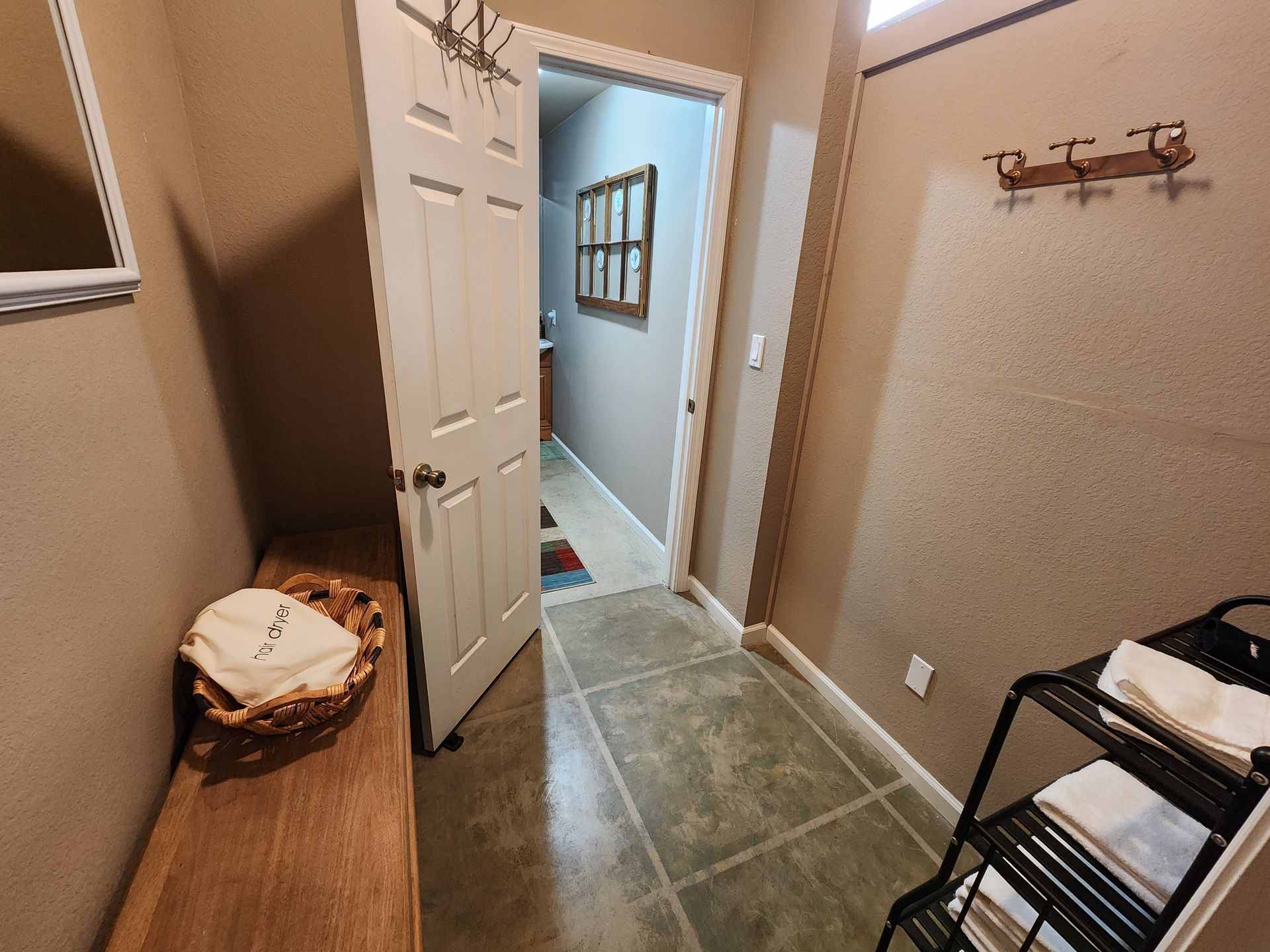 Entryway with bench, open door to hallway, towels on rack, coat rack on wall.