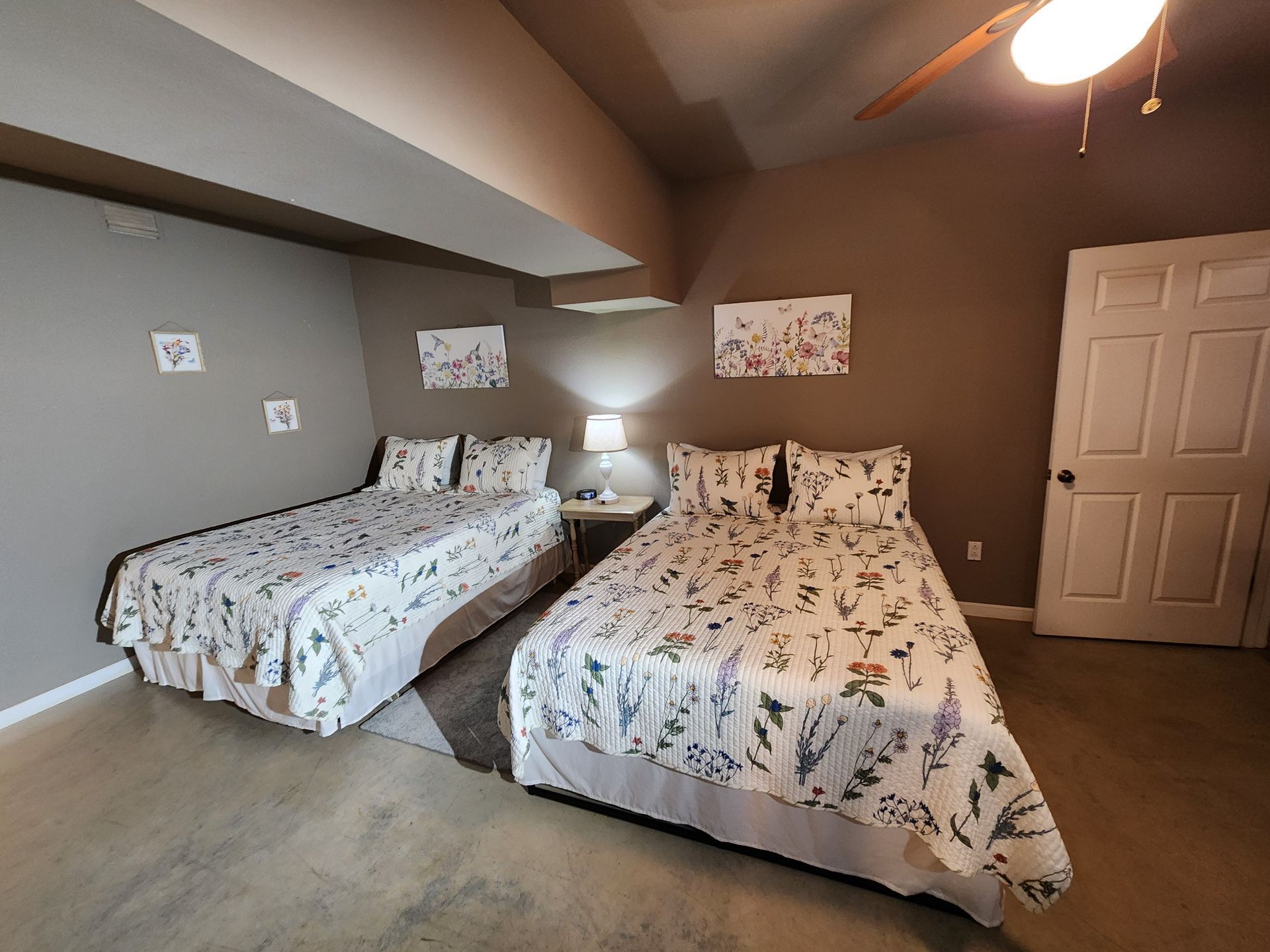 Two beds in a room with floral bedding, neutral walls, and a closed door.