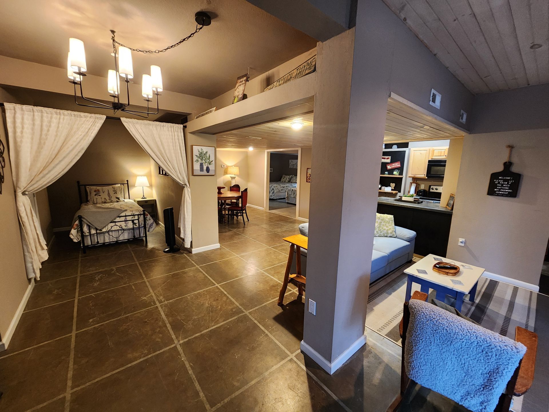 Open-concept apartment with bed area, dining, and living space; neutral tones, modern chandelier, tile floor.