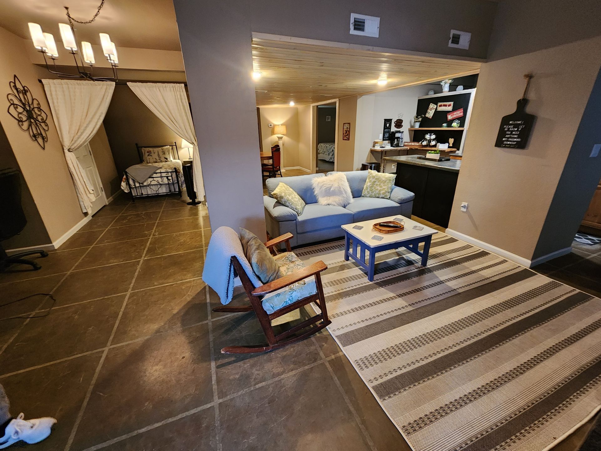 Open-concept living space with a blue couch, rocking chair, and a peek into a bedroom.