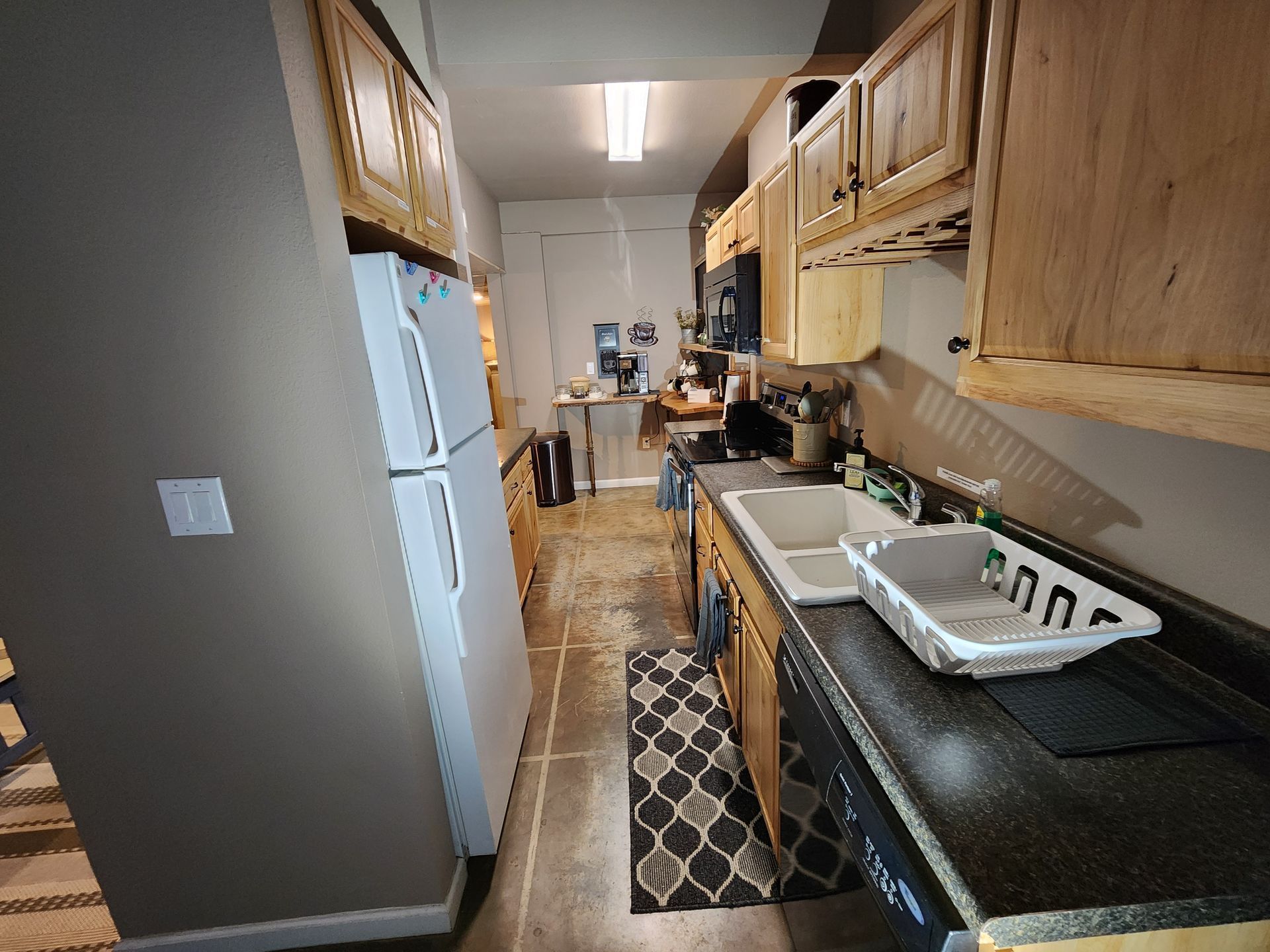 A narrow kitchen with a refrigerator, sink, cabinets, and appliances.