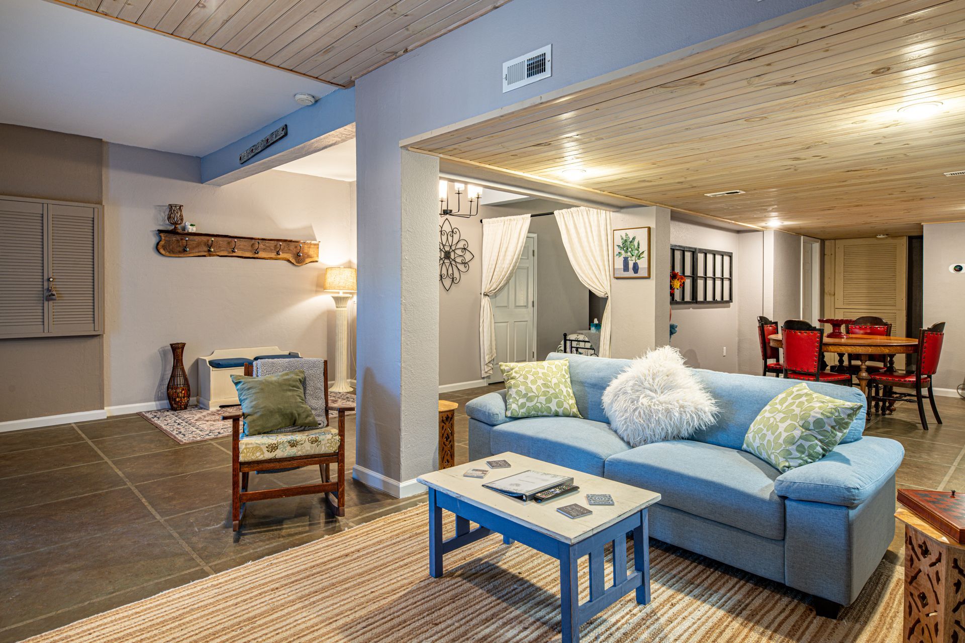 Living room with blue sofa, wooden ceiling, dining area, and neutral color scheme.