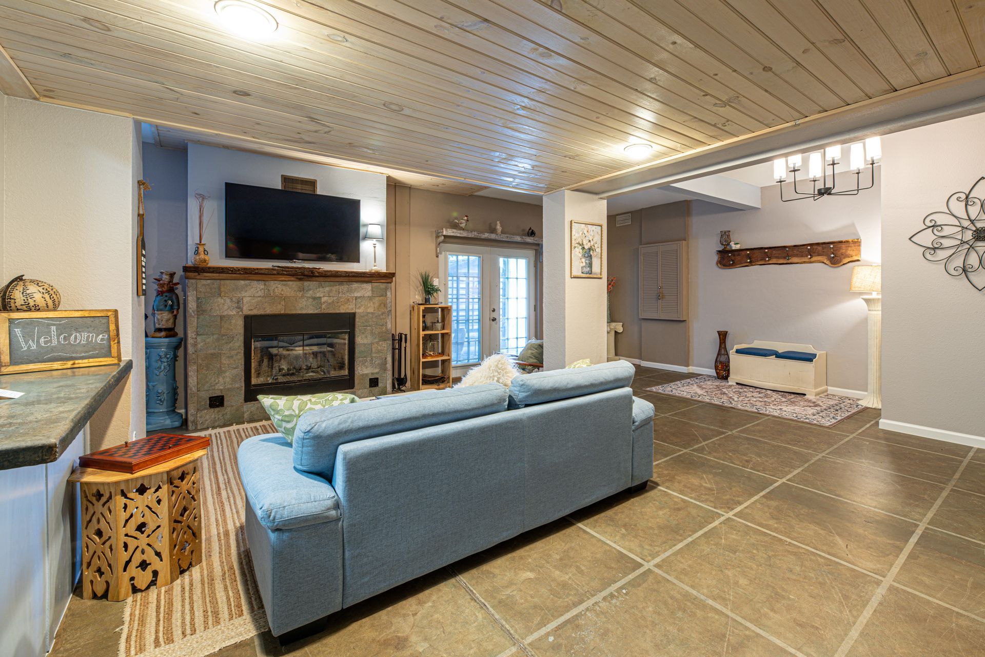 Living room with fireplace, blue sofa, stone floor, and light wood ceiling.