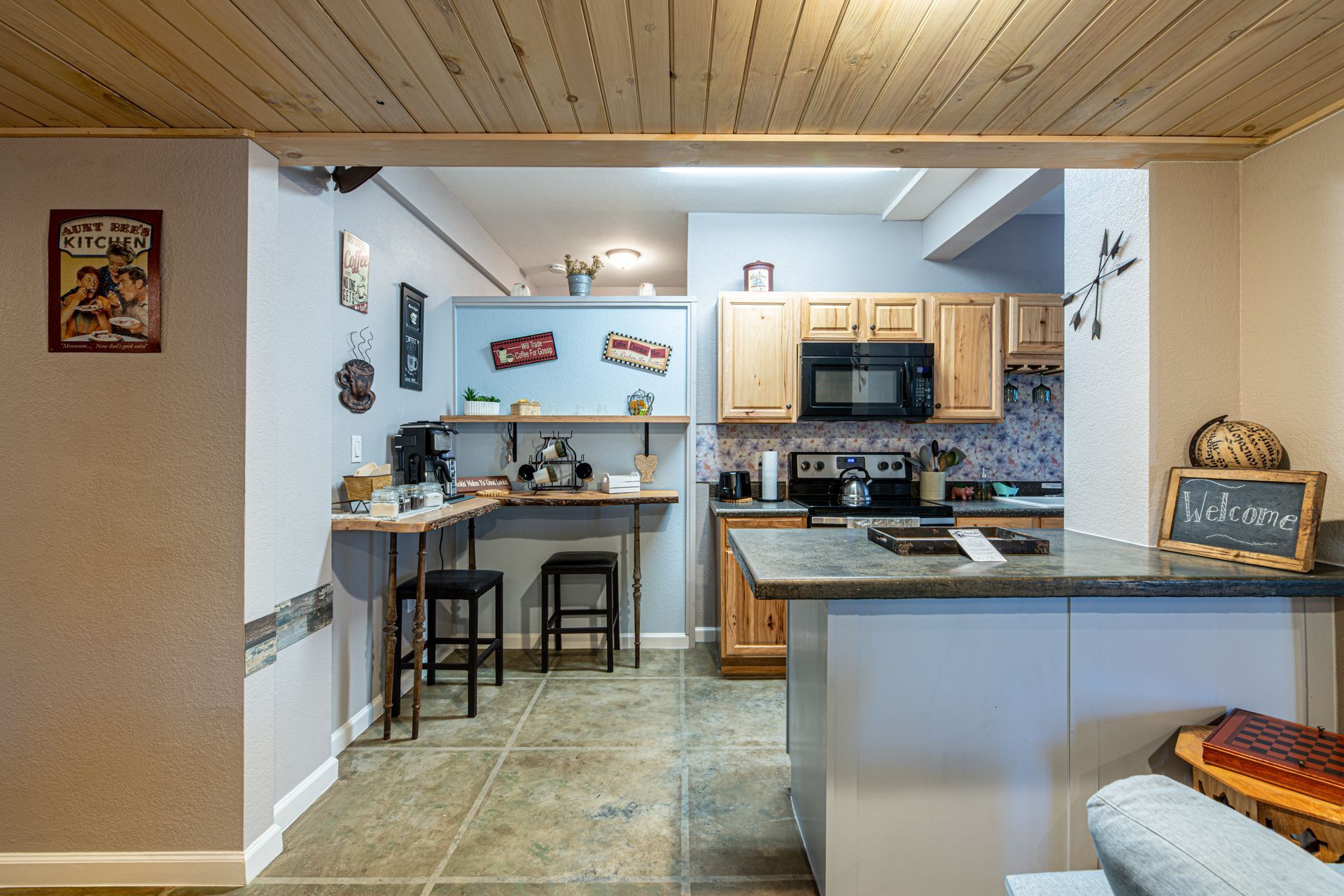 Kitchen with light wood cabinets, gray countertops, and a breakfast bar; visible brick accent wall and wood ceiling.