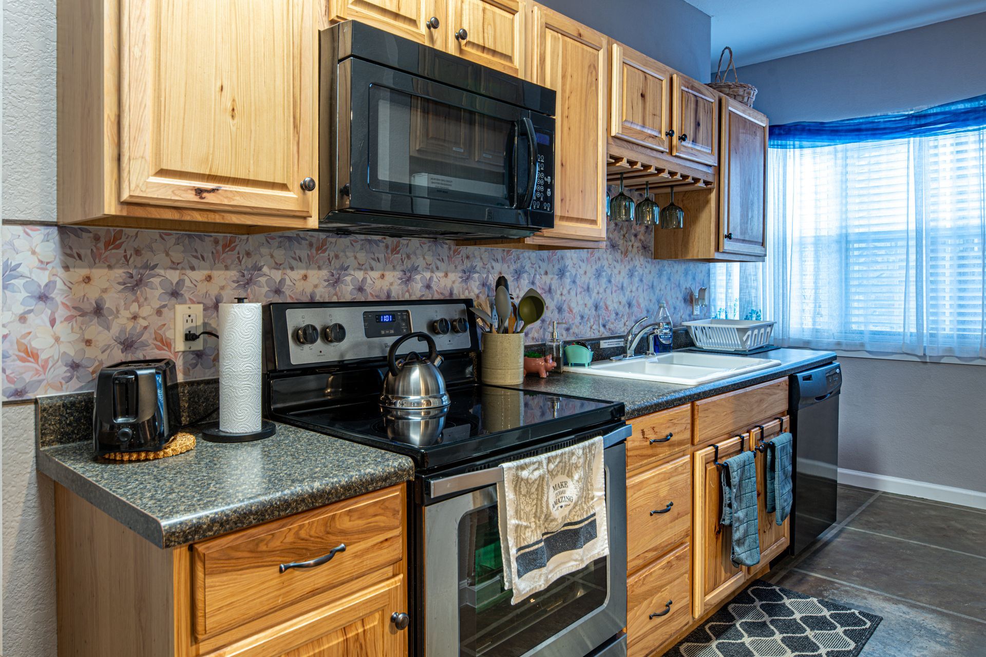 Kitchen with wood cabinets, black appliances, floral backsplash, and a window with blinds.